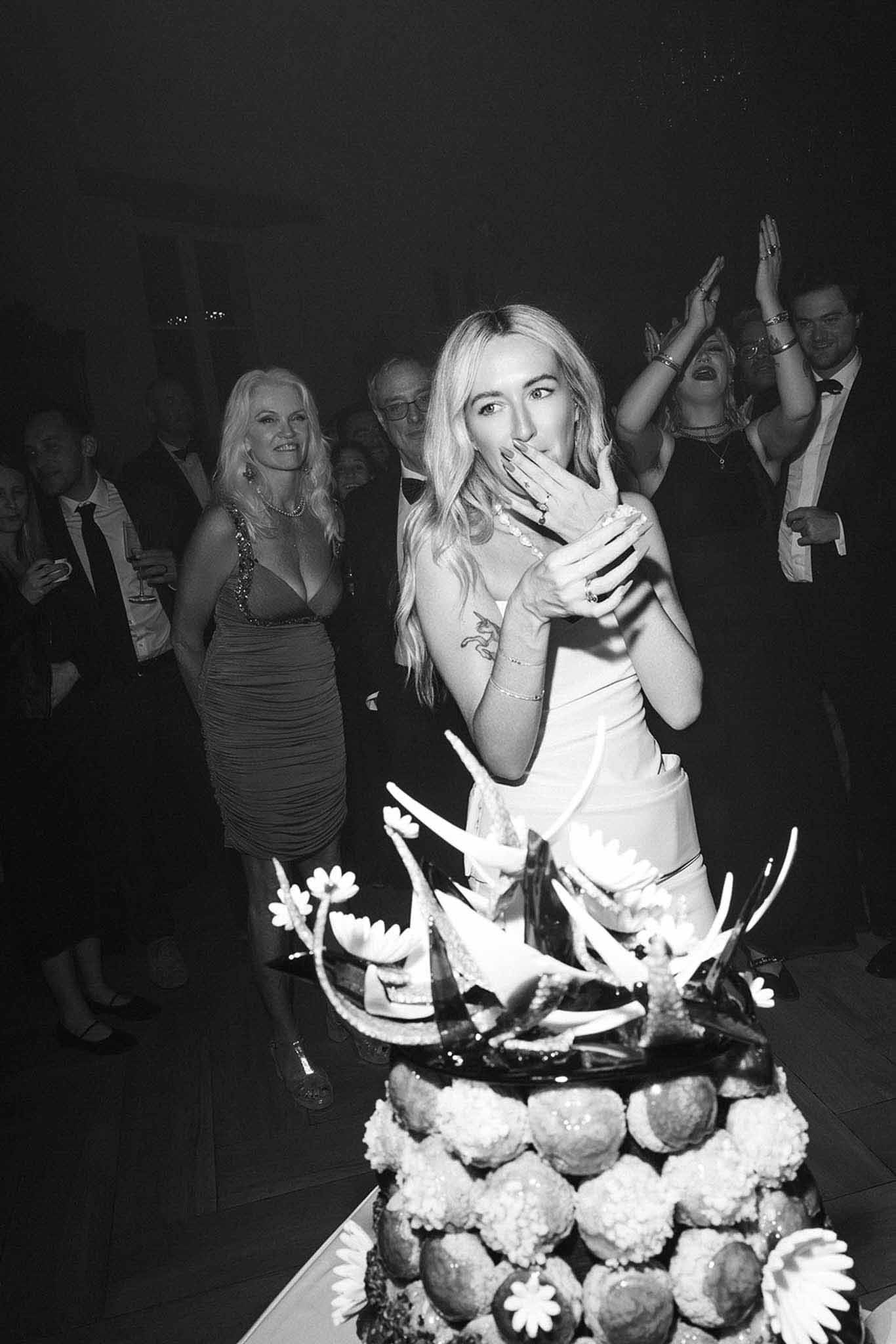 Black and white bride reacting with surprise at croquembouche cake cutting with laughing guests behind