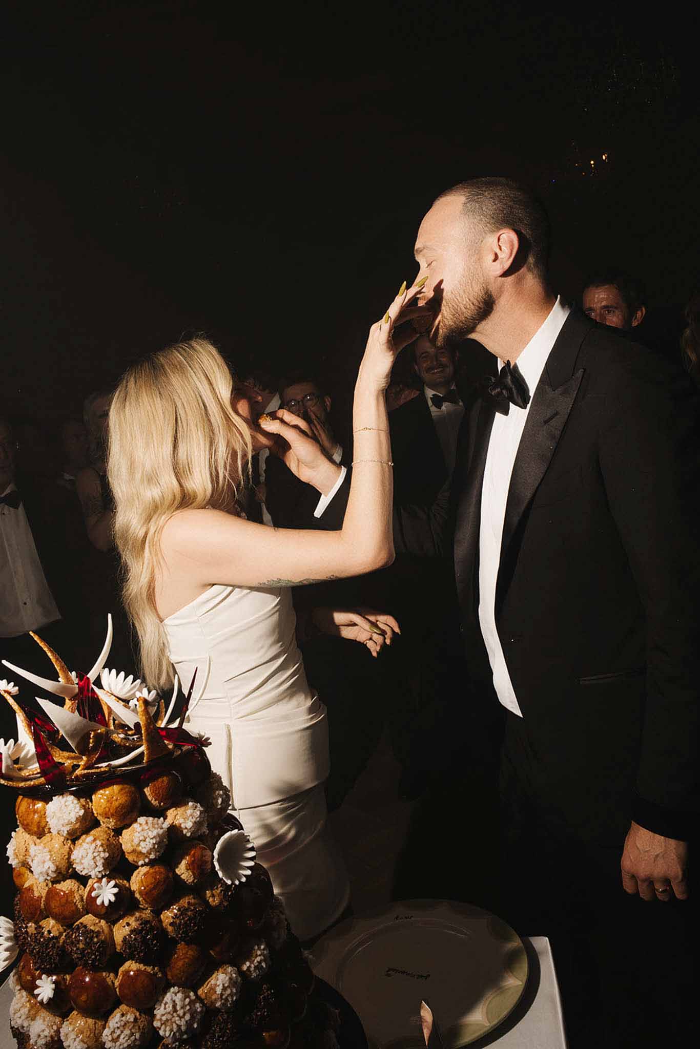 Bride feeds groom piece of croquembouche tower decorated with white chocolate and sugar flowers