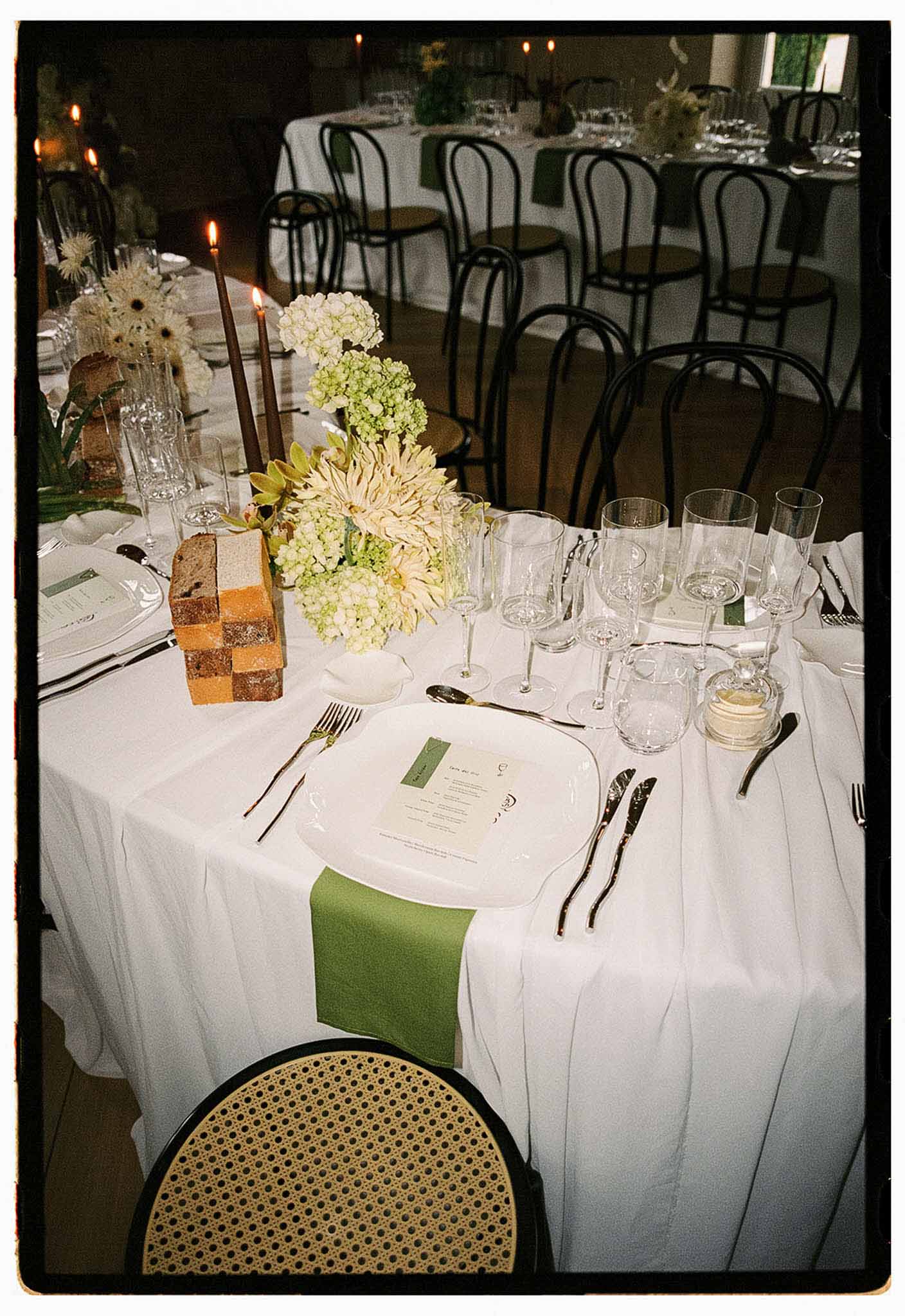 Reception table with cream dahlia centerpiece sage napkins burgundy taper candles and checkerboard bread