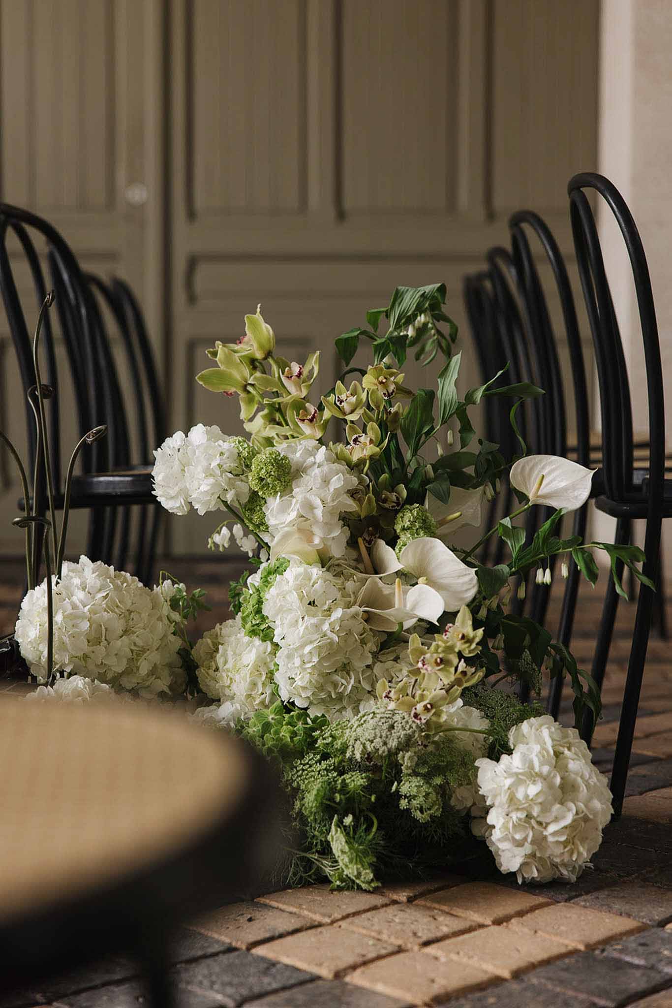Floor-level white hydrangea and green orchid floral arrangement on terracotta brick flooring with ceremony chairs