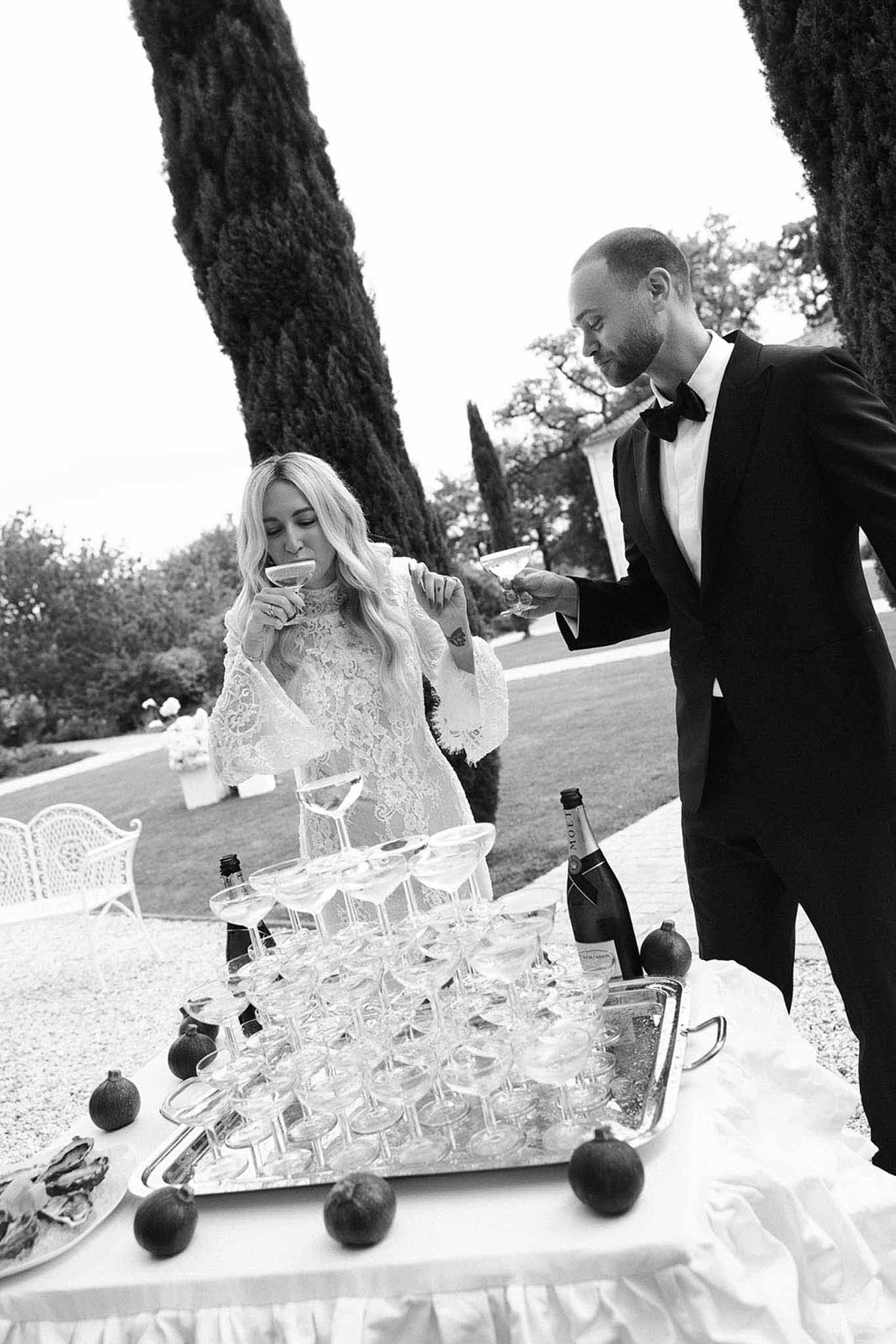Black and white couple sipping champagne beside coupe tower with oysters and figs on garden terrace