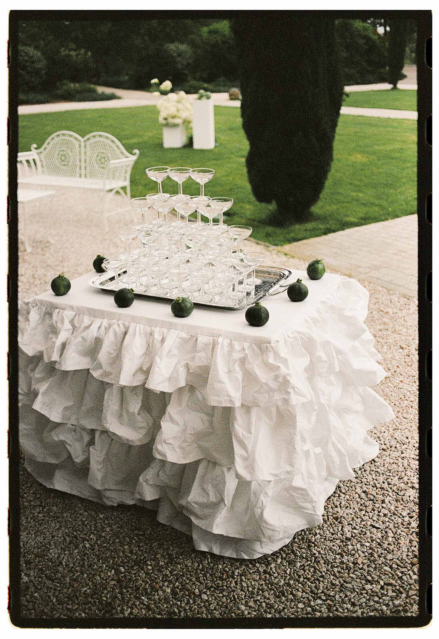Champagne coupe tower on ruffled white linen table with limes and hydrangea pedestal in formal garden