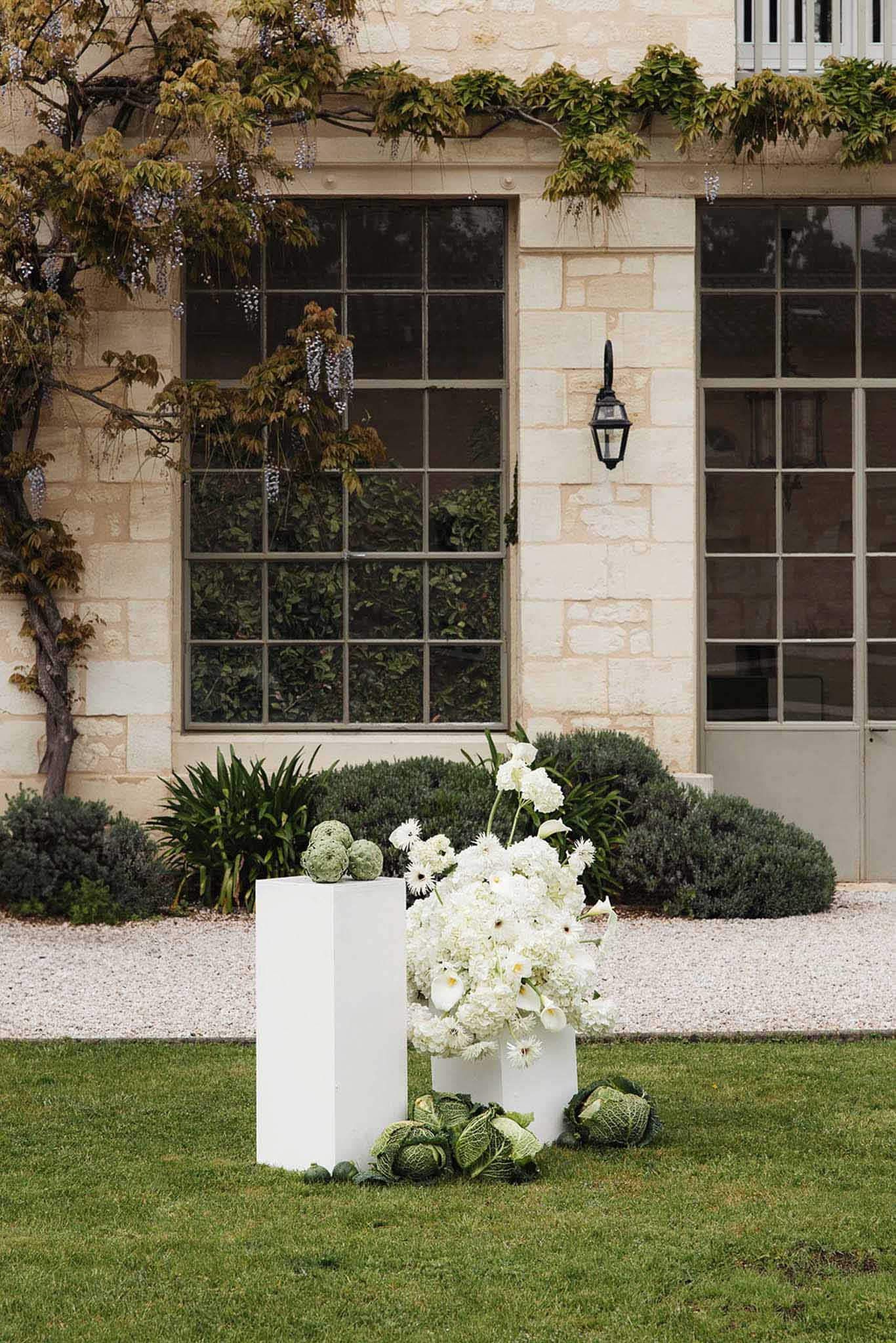 White floral arrangement on plinths with hydrangeas and calla lilies outside French limestone building