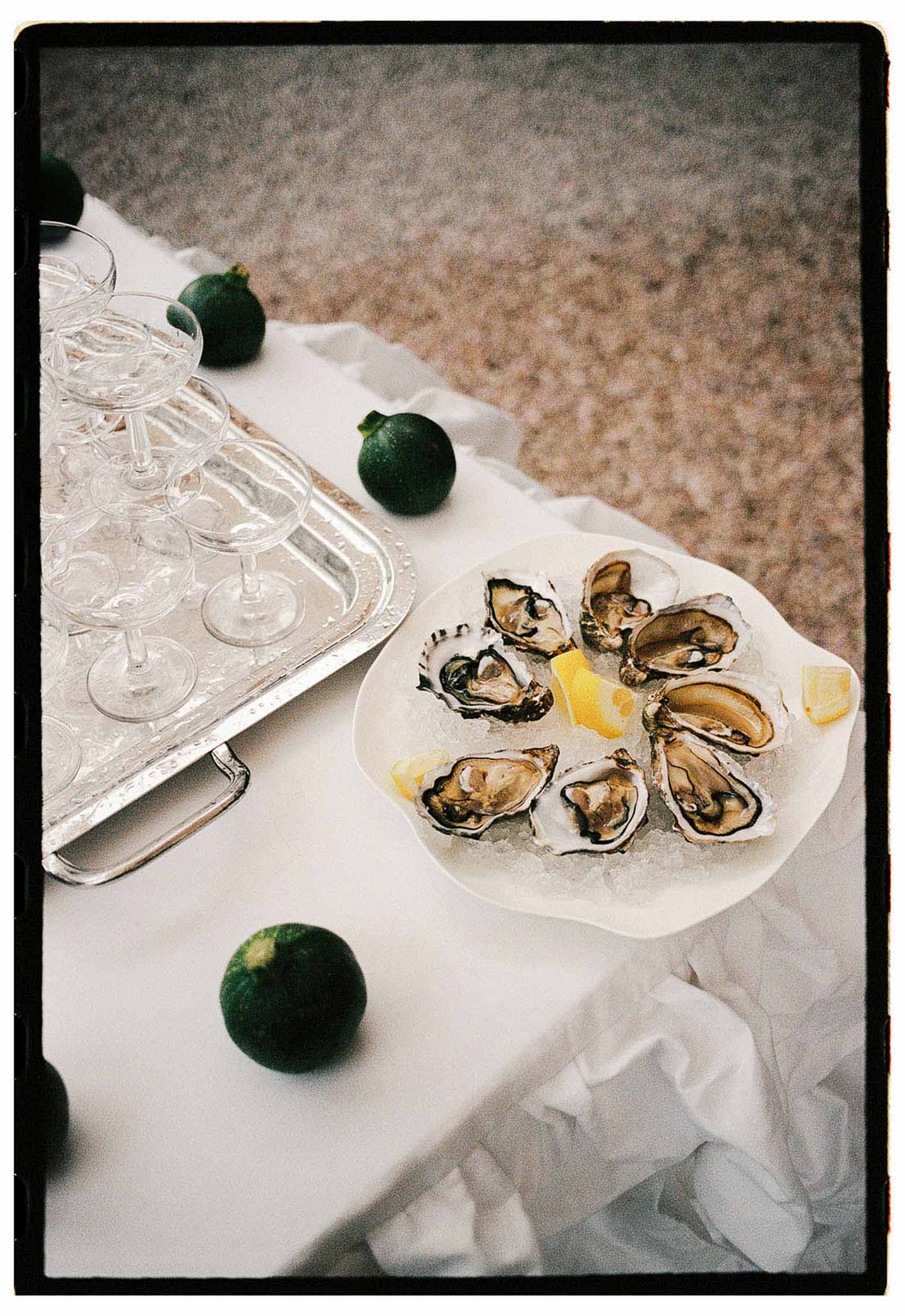 Freshly shucked oysters on crushed ice with lemon wedges and coupe glasses on a white linen table