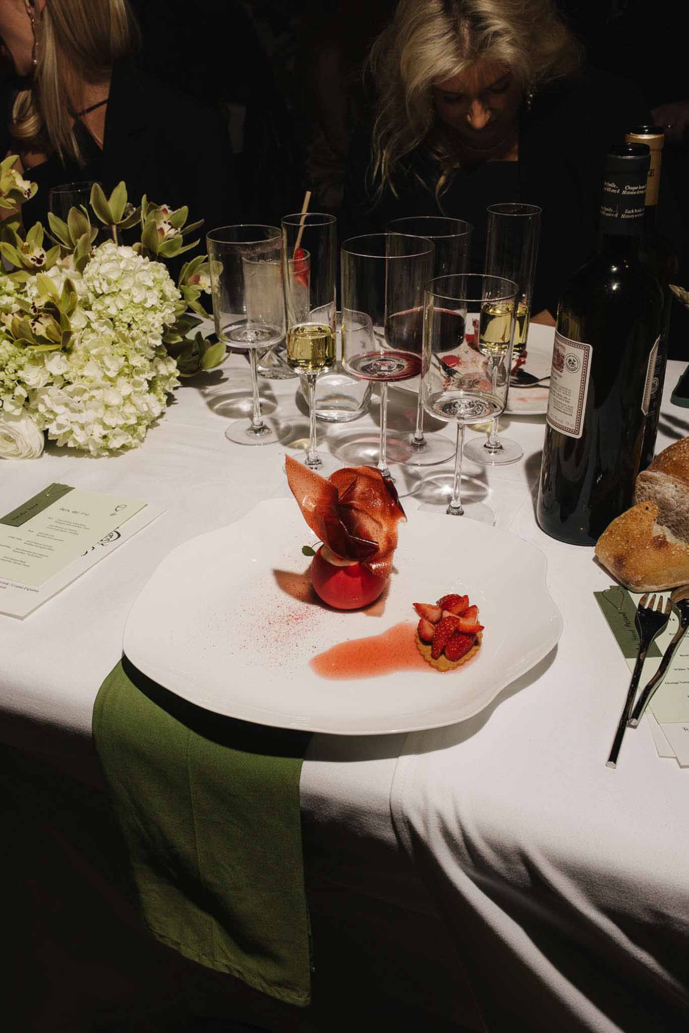 Plated dessert course with poached fruit and strawberry tartlet on a white scalloped plate at a reception table