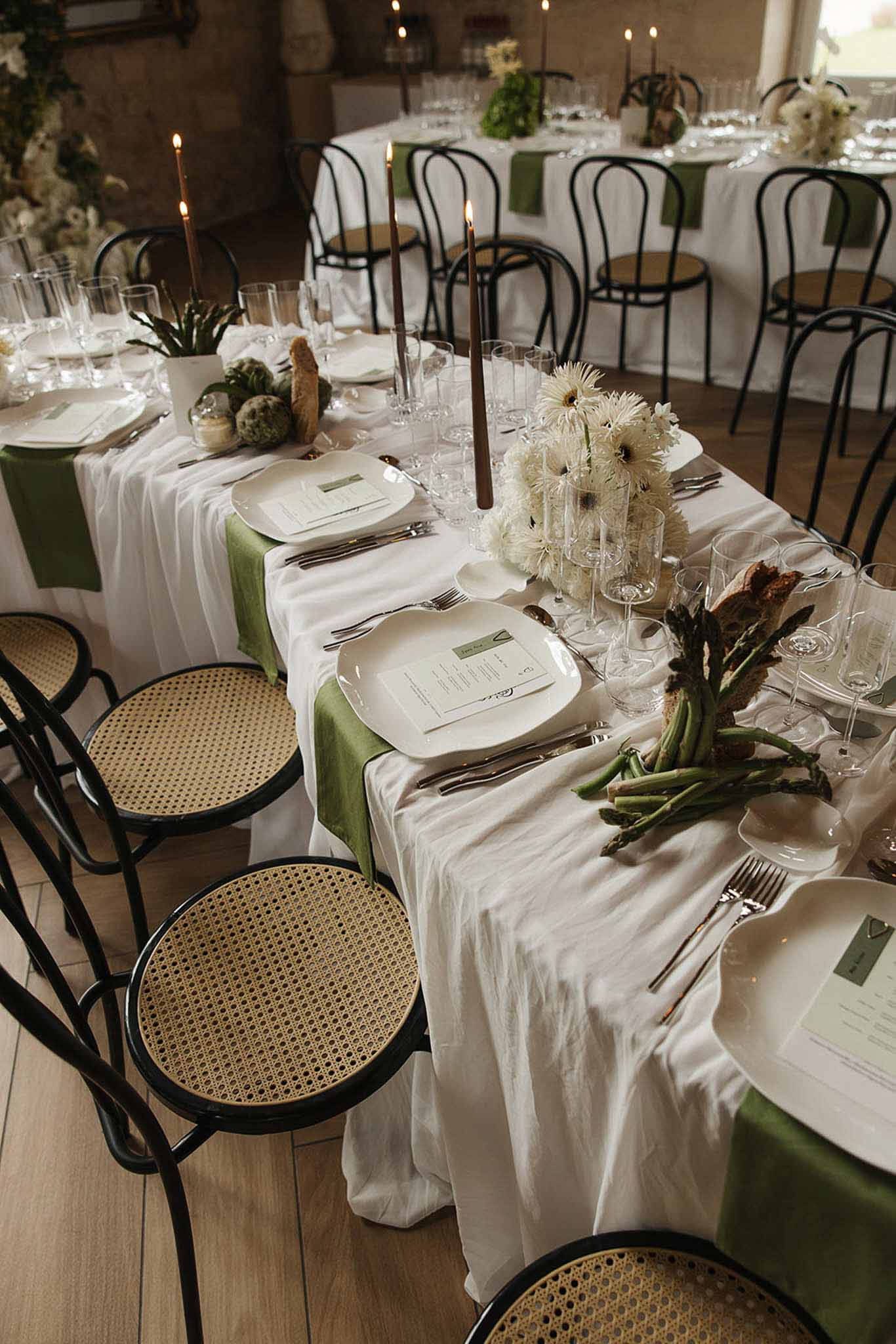 Reception tablescape with white gerbera daisies, olive napkins, brown taper candles, and asparagus accents