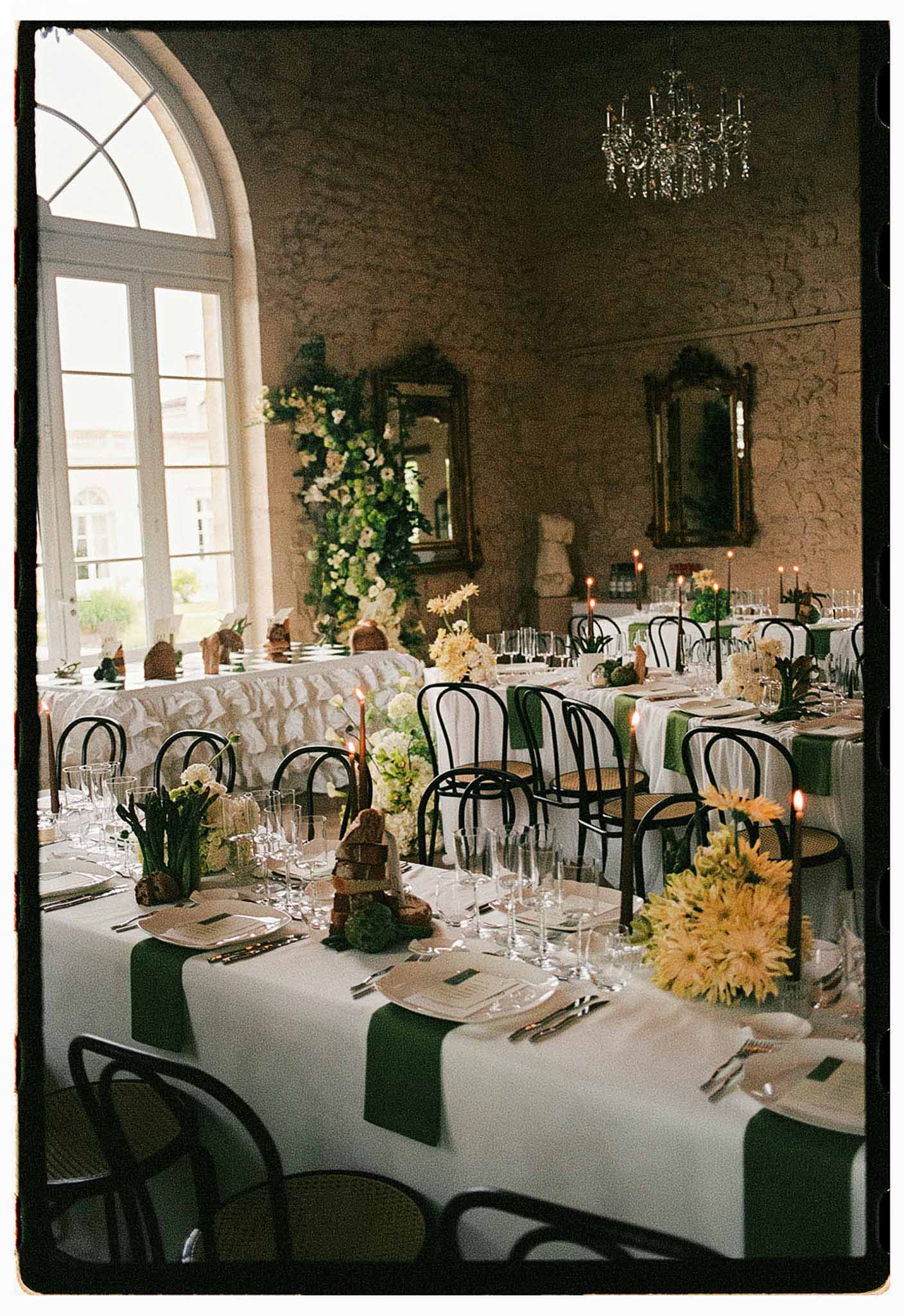 Chateau reception with black bistro chairs green napkins yellow daisy centerpieces and cascading white floral installation
