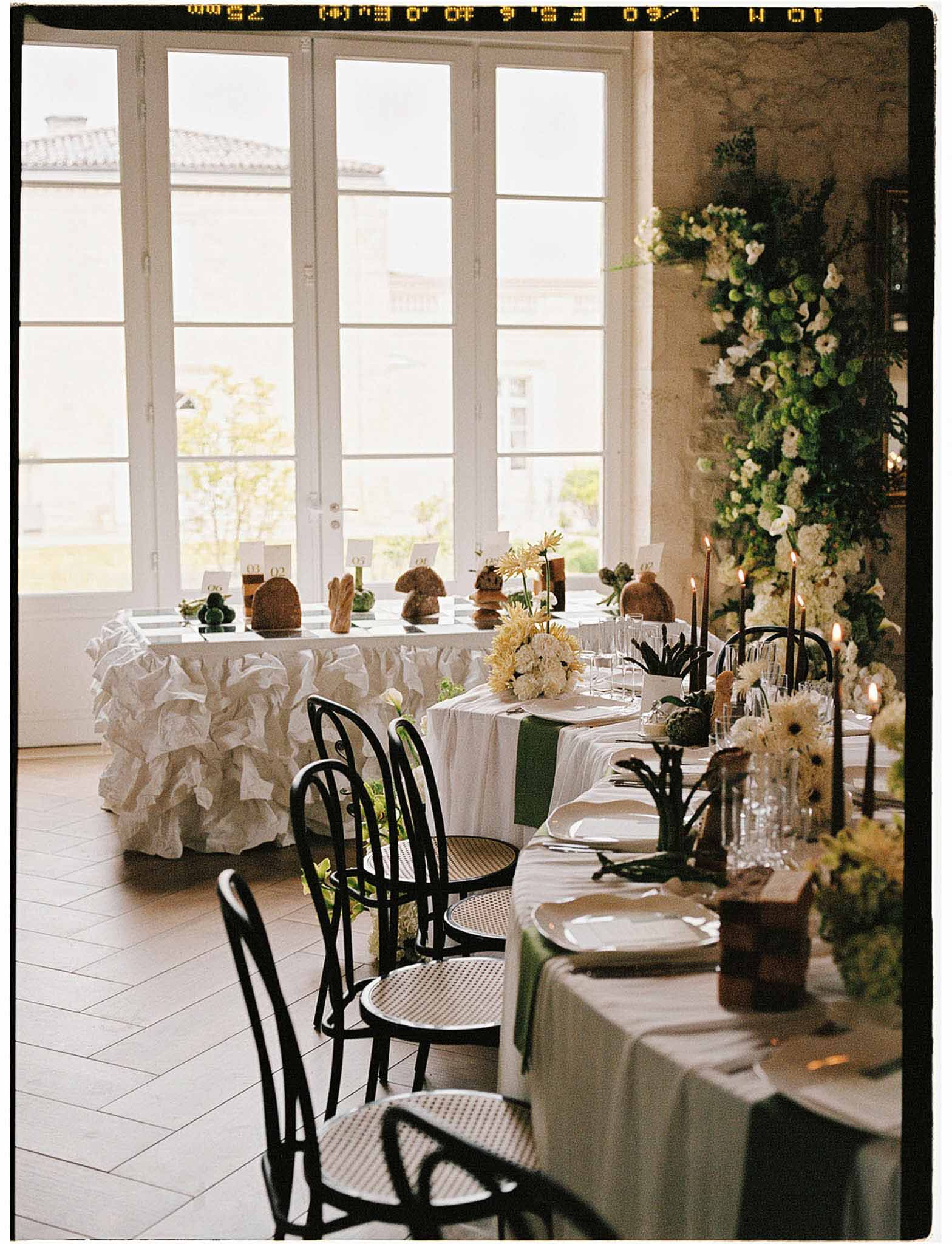 Reception tablescape in French chateau with white dahlias, yellow gerberas, black taper candles and vertical floral instal...