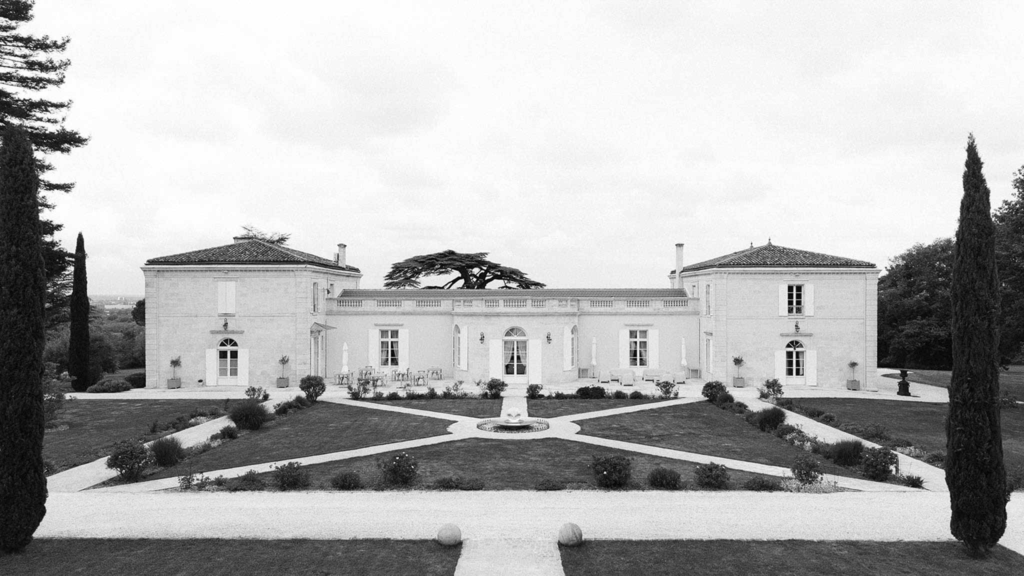 Black-and-white aerial view of a neoclassical French chateau with formal geometric gardens and fountain