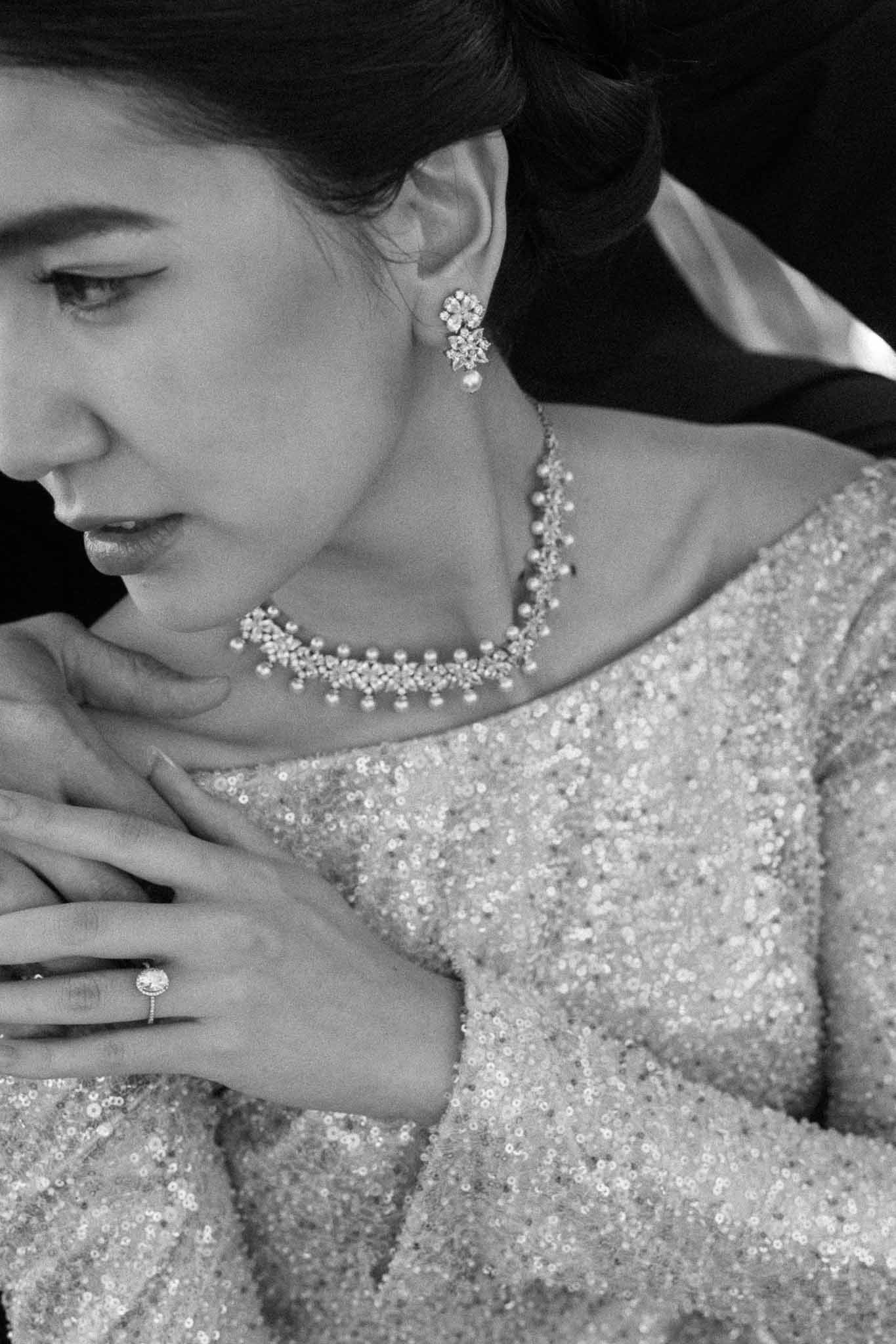 Black and white close-up of bride with sequined gown, pearl cluster earring, scalloped crystal necklace, and diamond ring