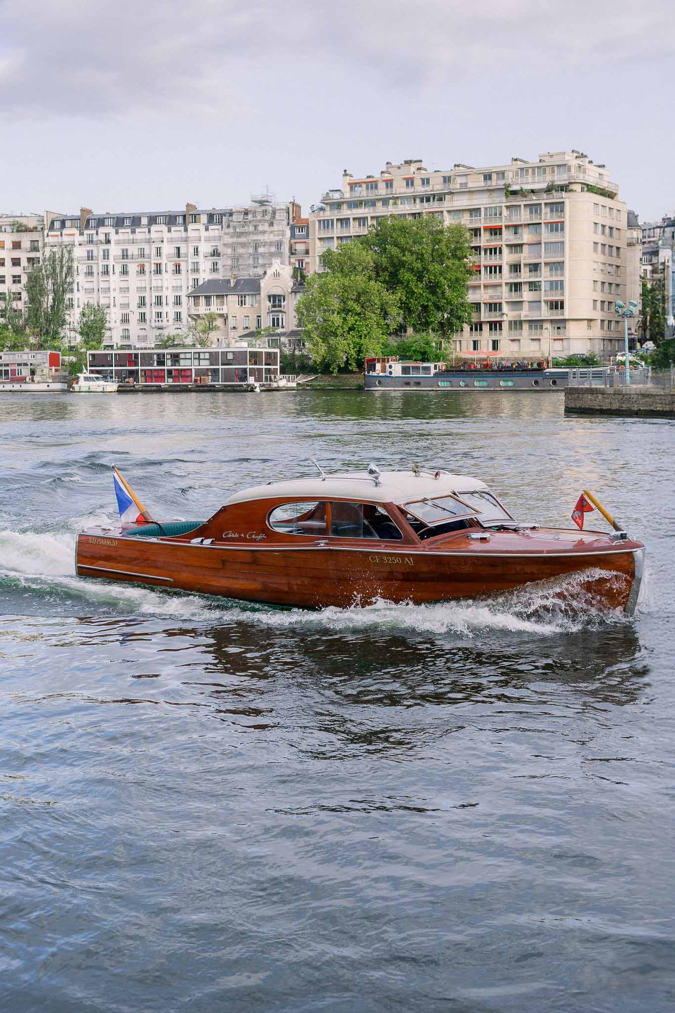 Vintage mahogany motorboat with French tricolor cruises the Seine past Haussmann buildings in Paris