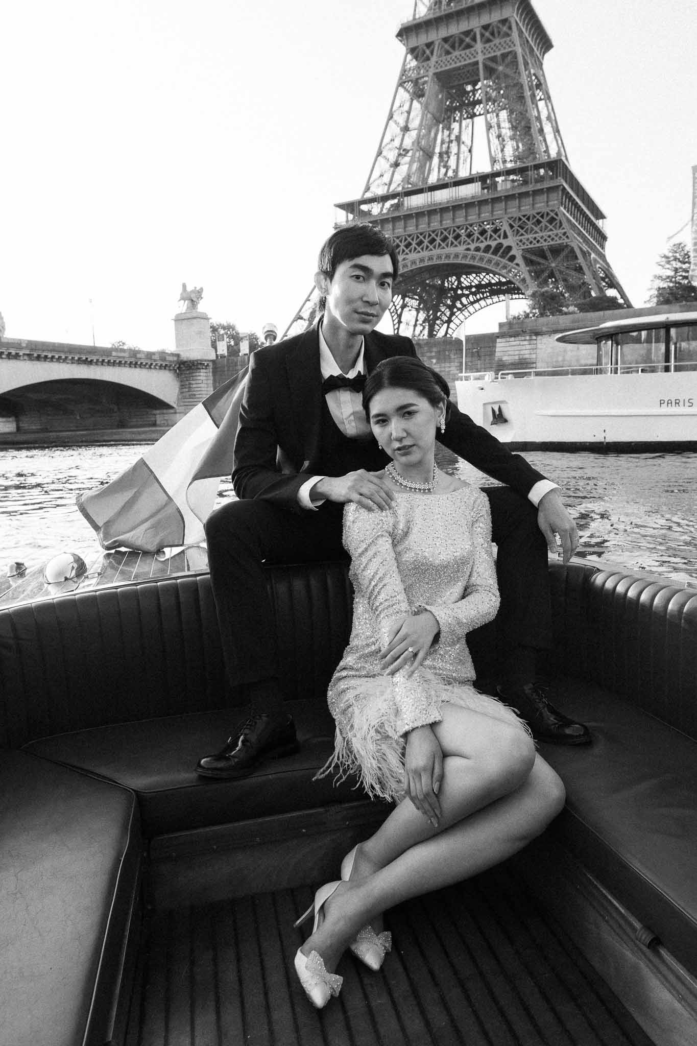 Black and white portrait of bride and groom seated on a boat on the Seine with Eiffel Tower in background