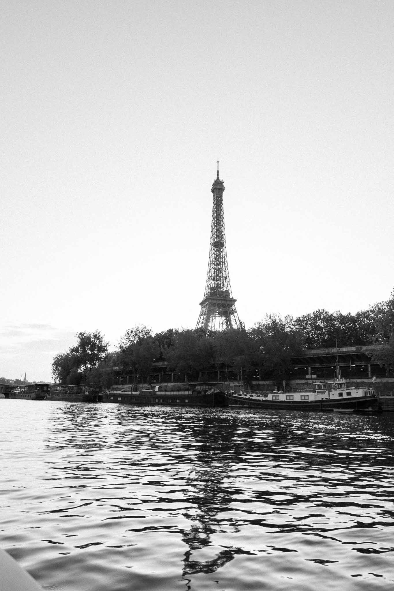 Black and white Seine River view with Eiffel Tower, moored barges, and tree-lined quayside