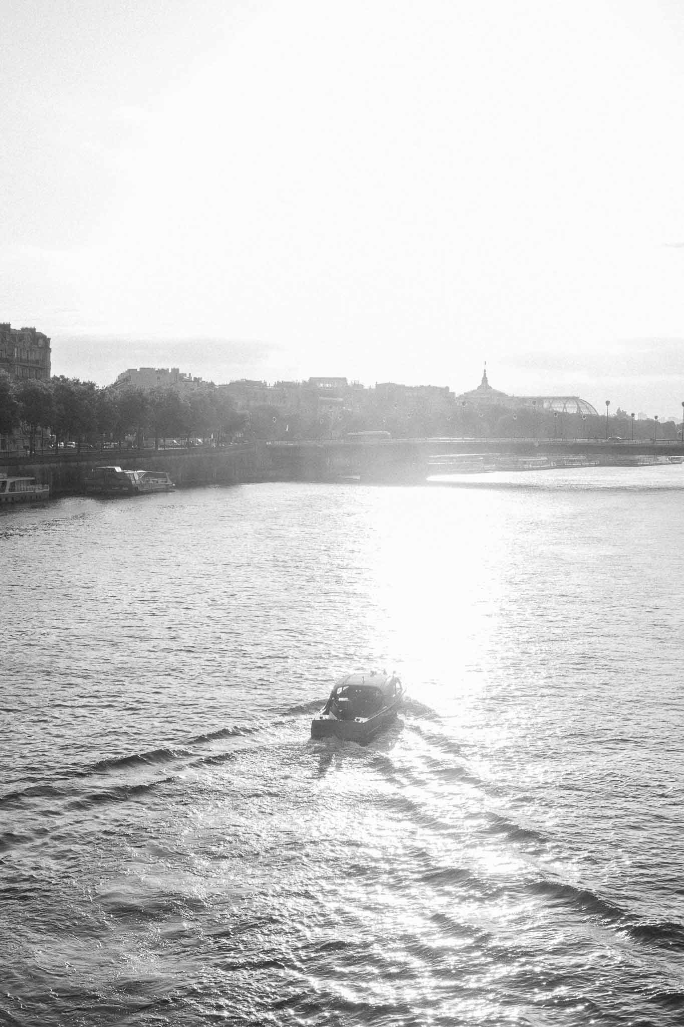 Black and white Seine River scene with motorboat wake and Haussmann buildings on distant bank