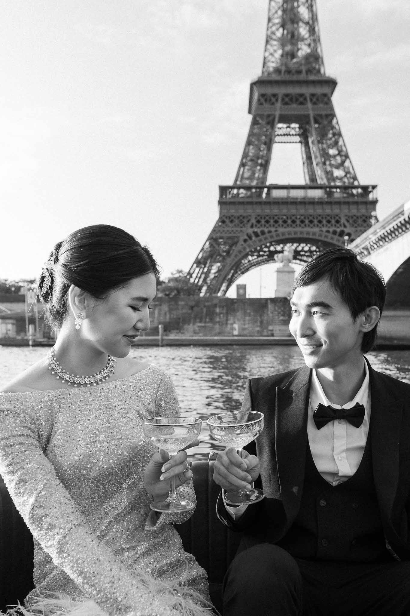 Black and white couple toasting champagne coupes beside the Seine with Eiffel Tower behind