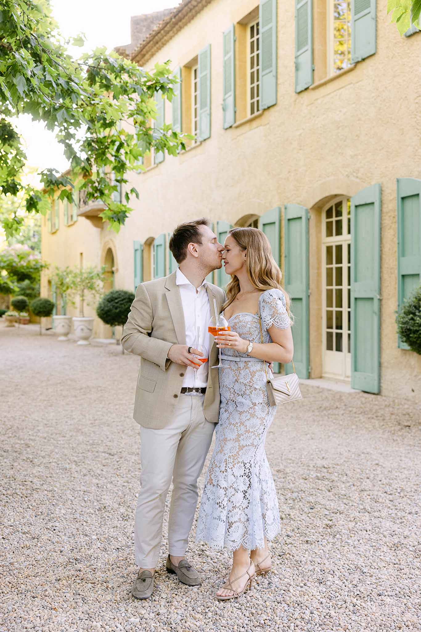 Couple kissing with Aperol Spritz cocktails at Provencal manor with ochre walls and green shutters