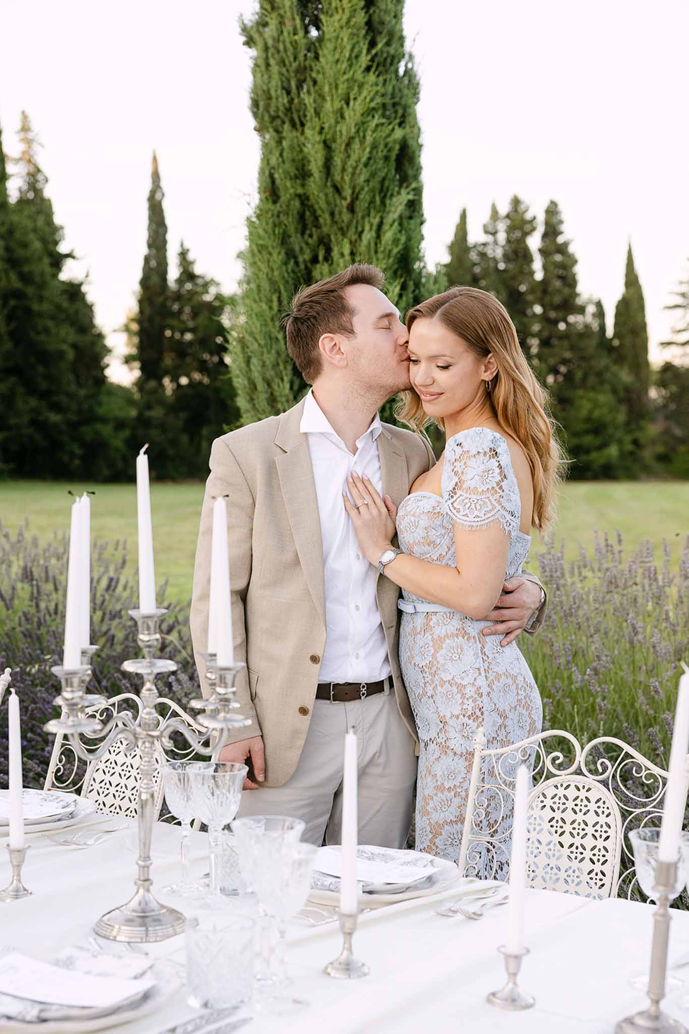 Couple beside silver candelabra table in lavender rows with cypress trees and white chairs at dusk