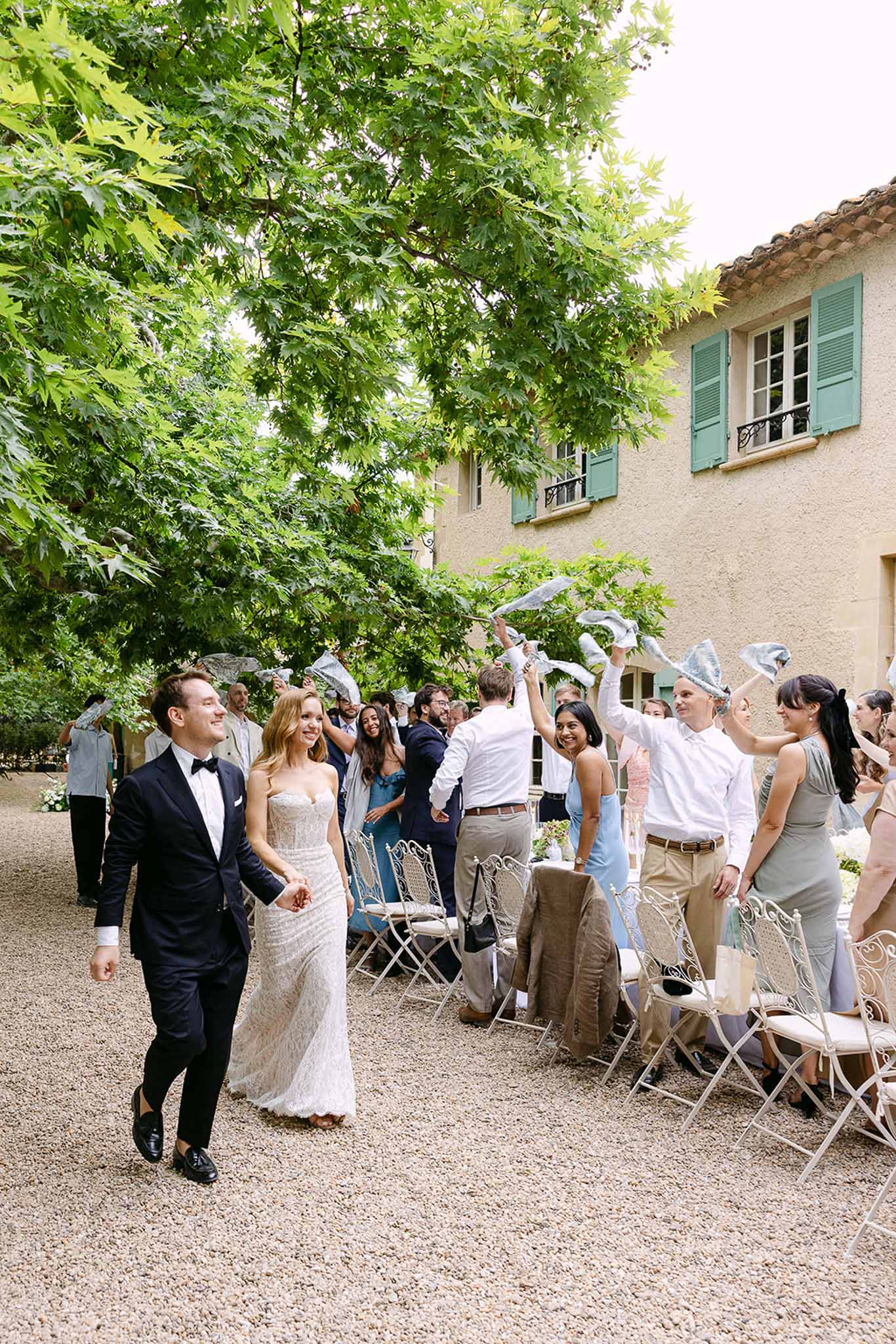 Bride and groom exit through guests waving metallic ribbon fans at Provencal mas courtyard