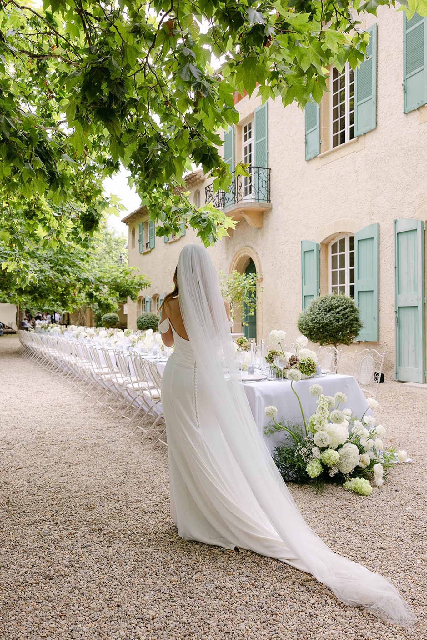 Bride with cathedral veil facing an outdoor reception table with white hydrangeas at a Provencal manor house