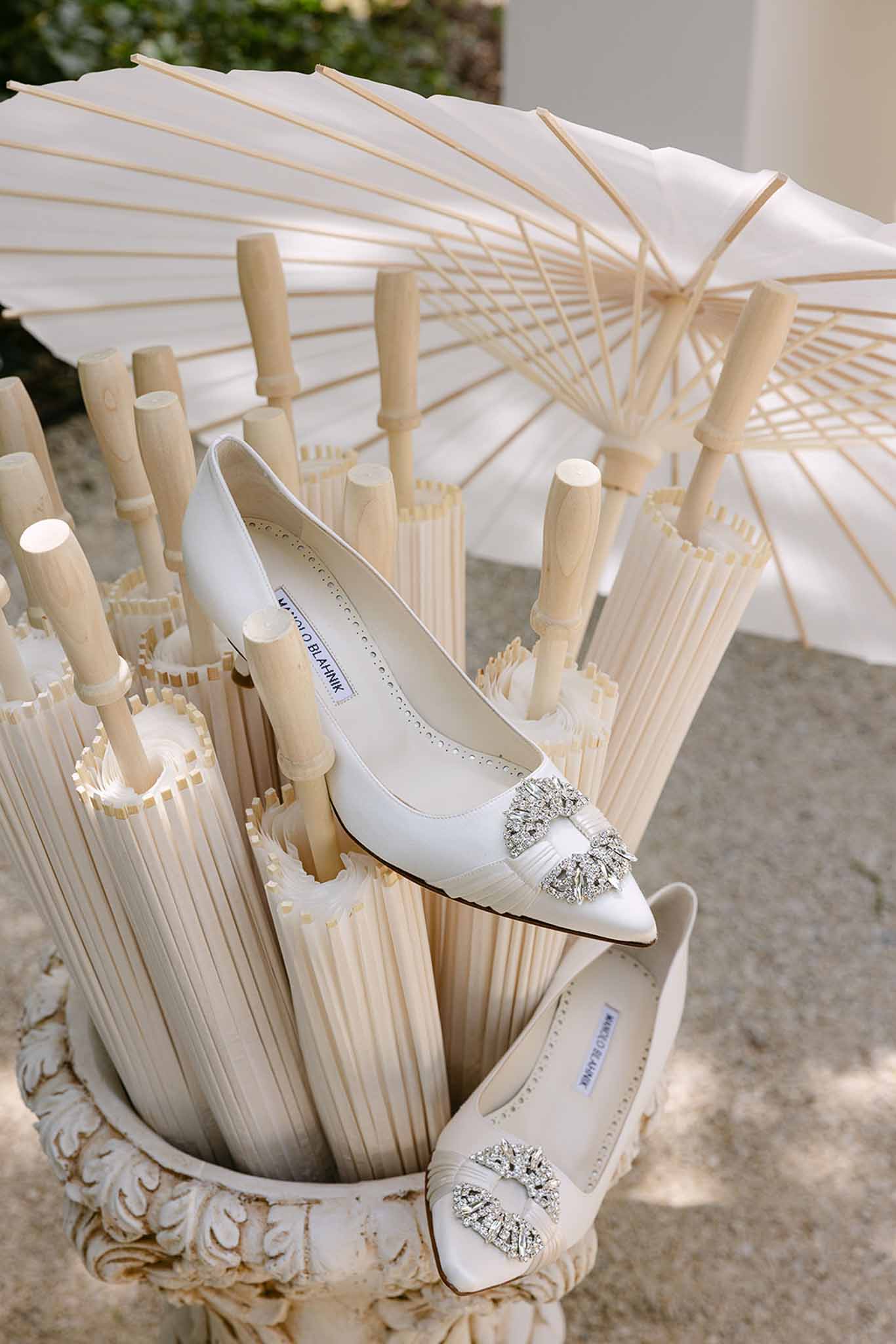 White Manolo Blahnik bridal flats with crystal buckles placed among white paper parasols in plaster stand