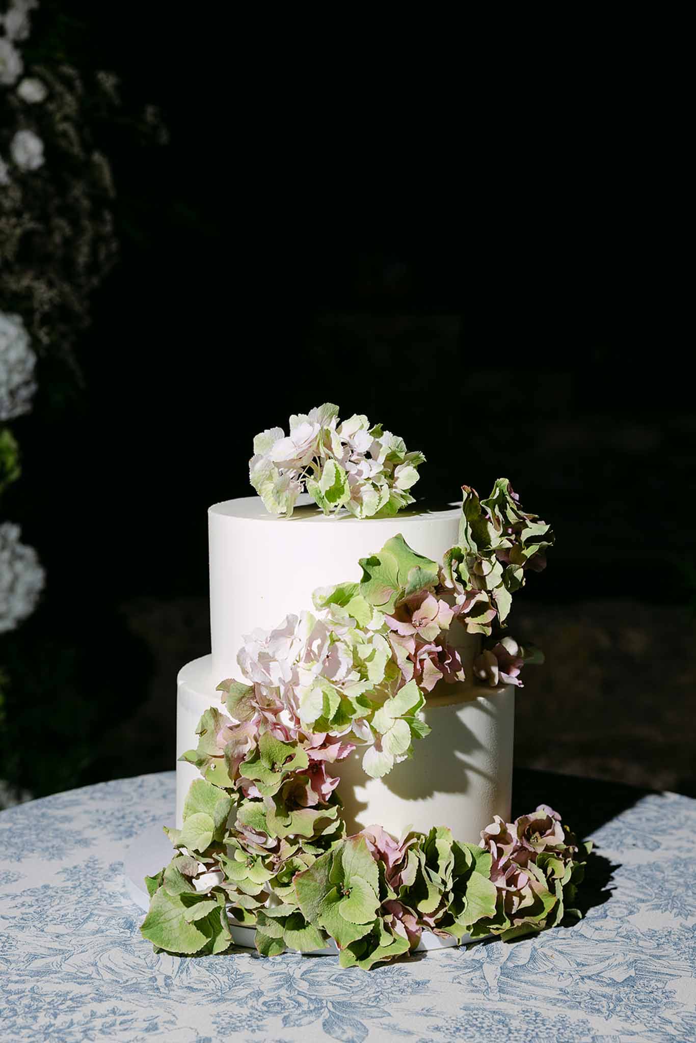 Two-tier white cake with cascading dried dusty pink hydrangea on blue toile de Jouy linen
