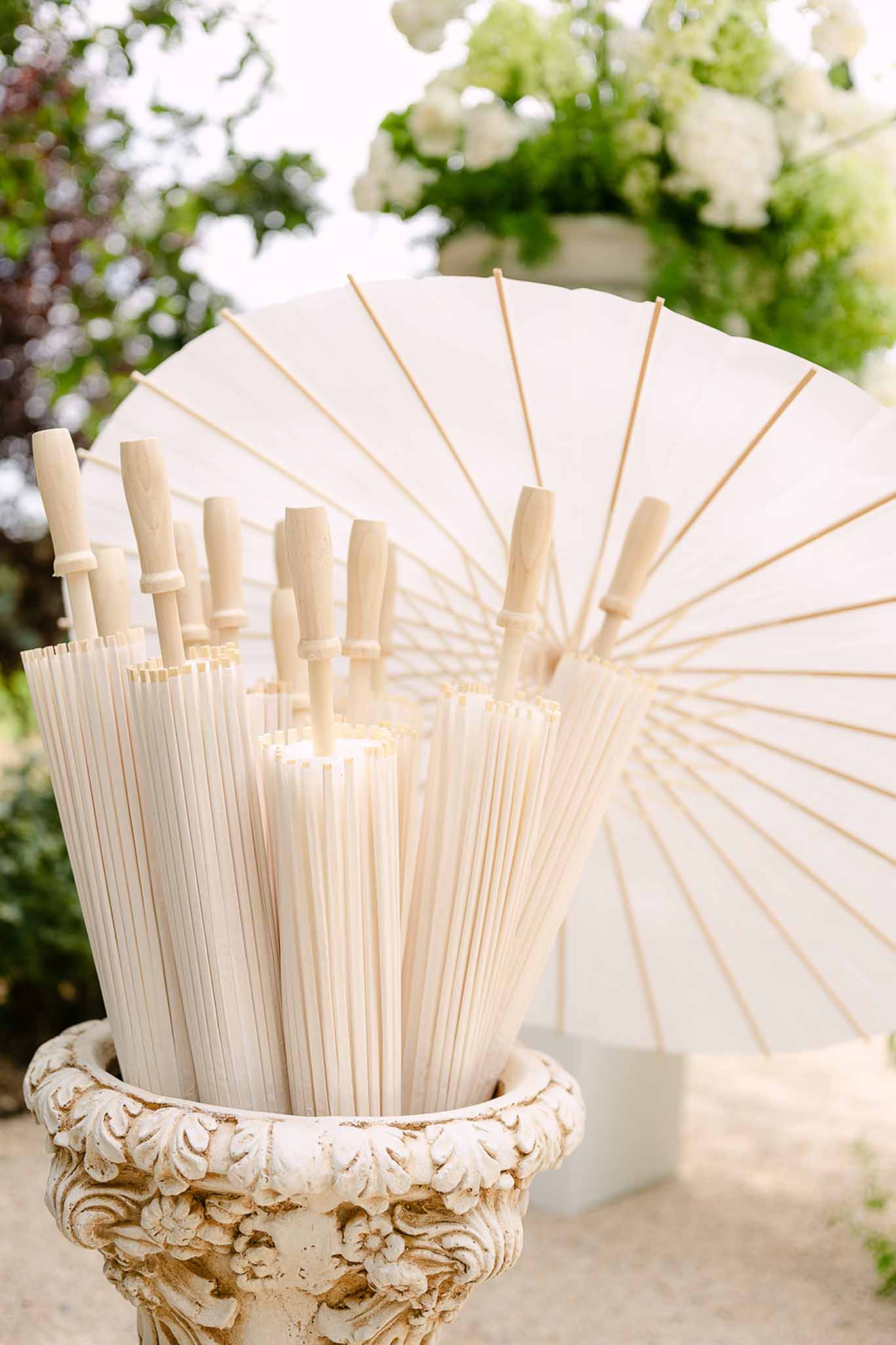 White paper parasols displayed upside-down in carved stone urn with white hydrangeas in garden setting