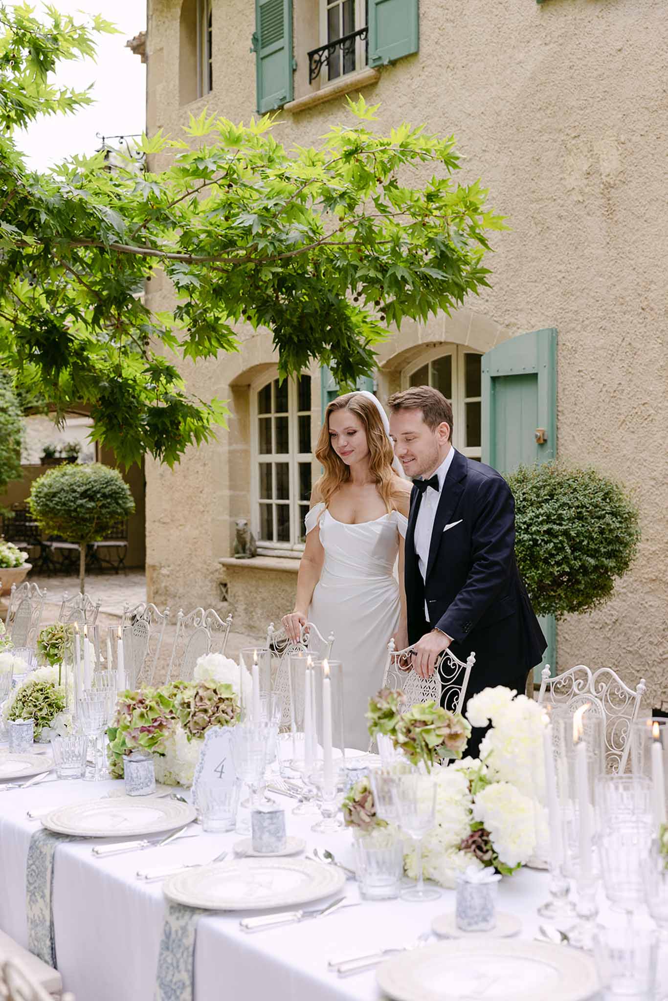 Couple at reception table with blue runner, white hydrangea centerpieces, and bistro chairs