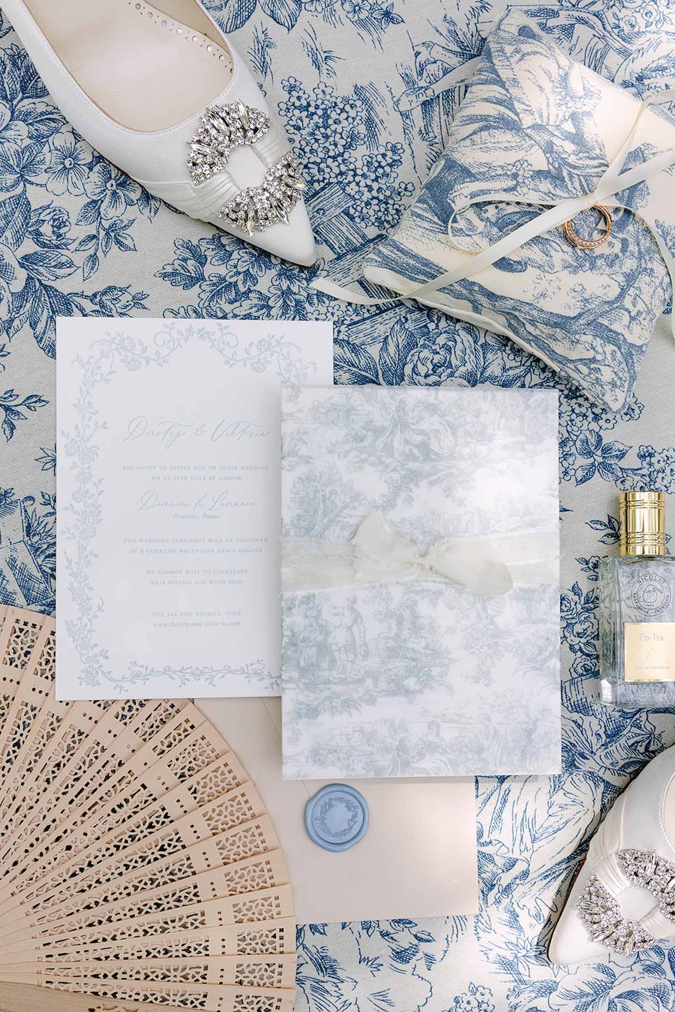 Toile de Jouy themed stationery flat lay with blue wax seal, ivory satin heels, and gold rings