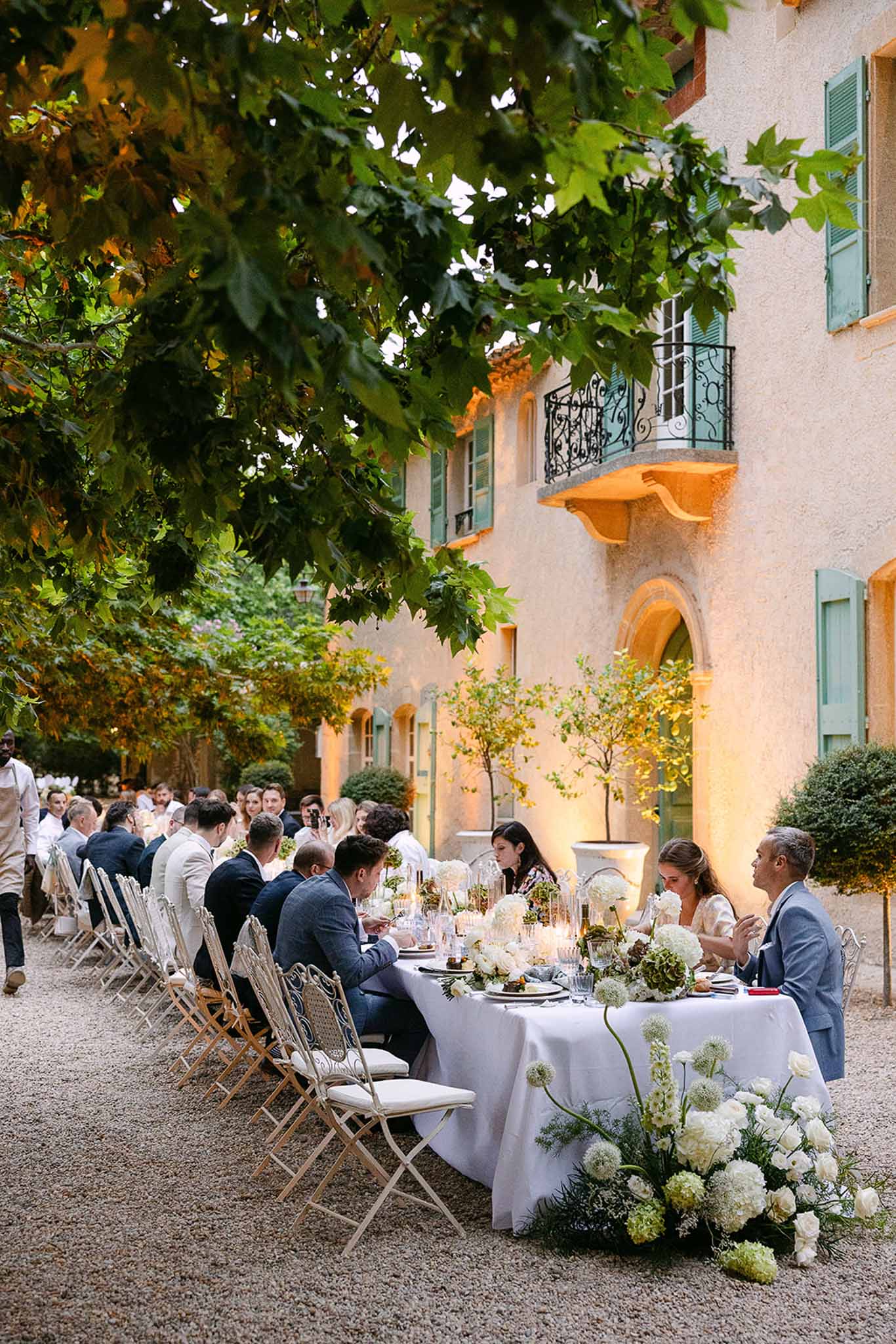 Long feasting table with white hydrangea runner and cascading florals before ochre Provencal manor