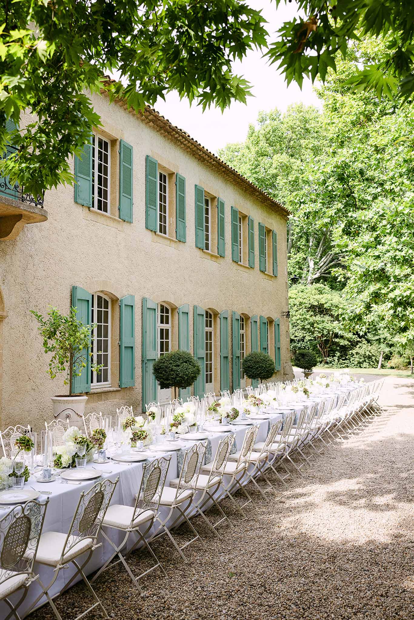 Long banquet table with white hydrangea centerpieces topiary and metal chairs along ochre Provencal bastide facade