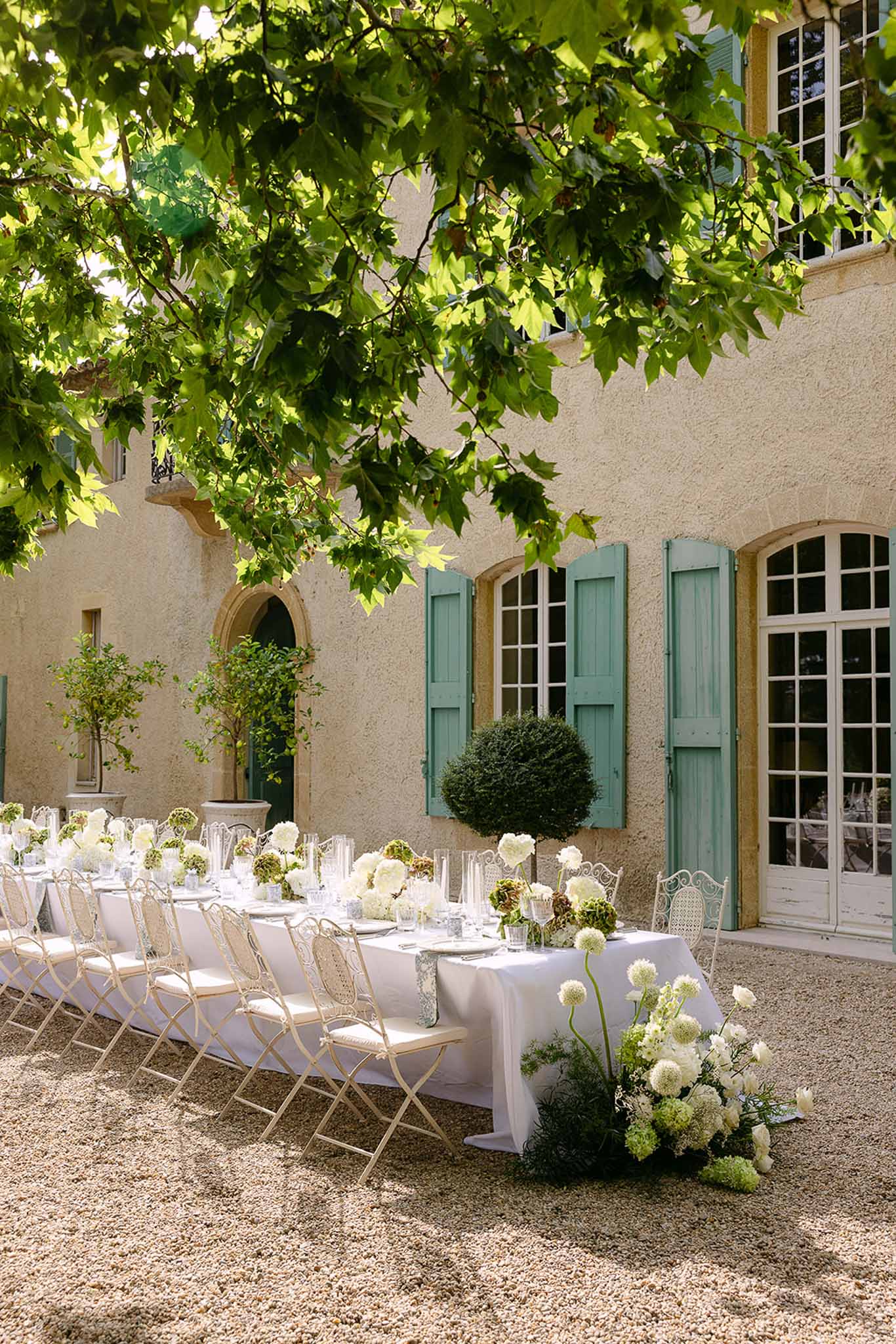 Long feasting table with white hydrangeas and green arrangements on gravel courtyard at Provencal bastide