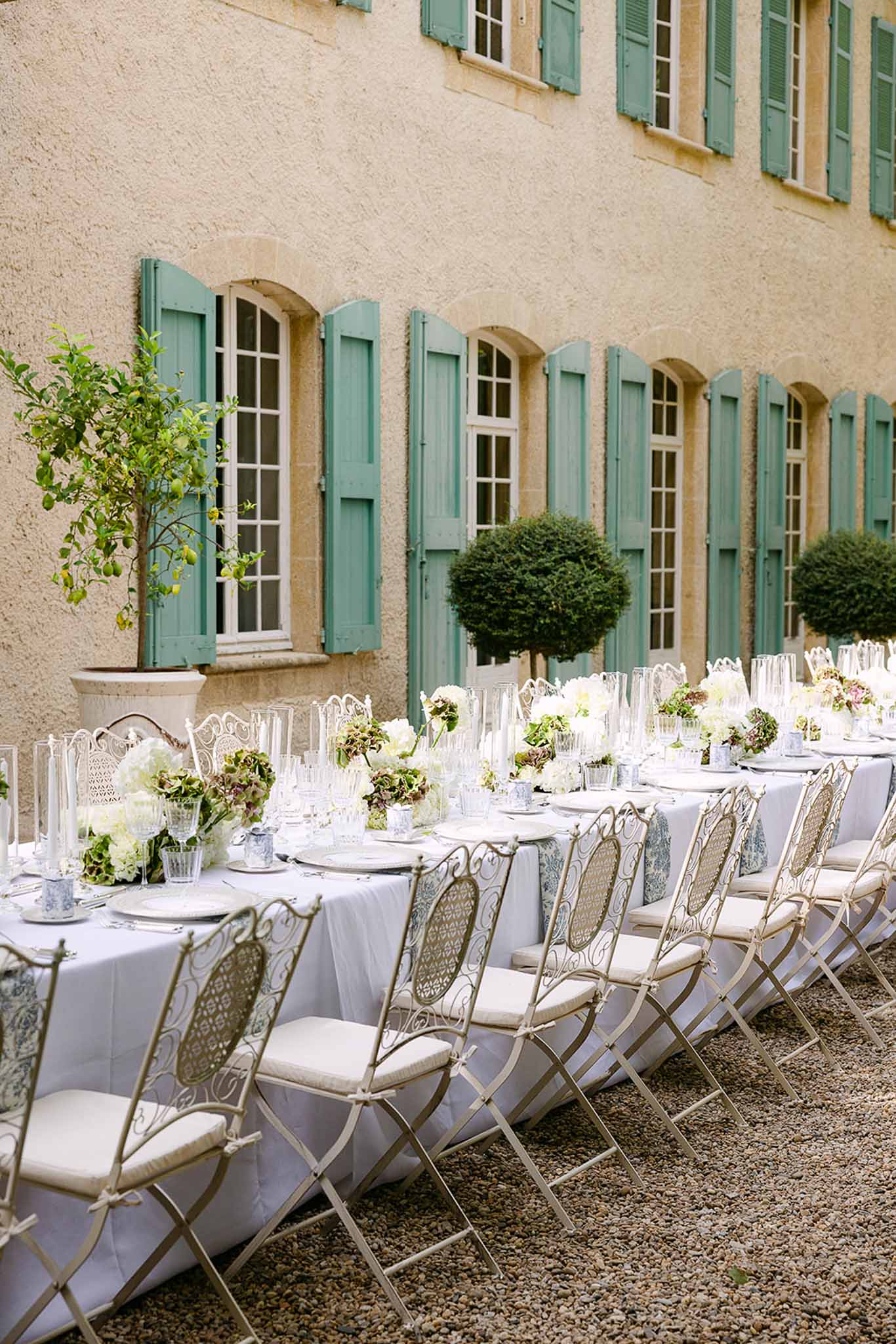 Long banquet table with hydrangea centerpieces and hurricane candles set against French manor with green shutters