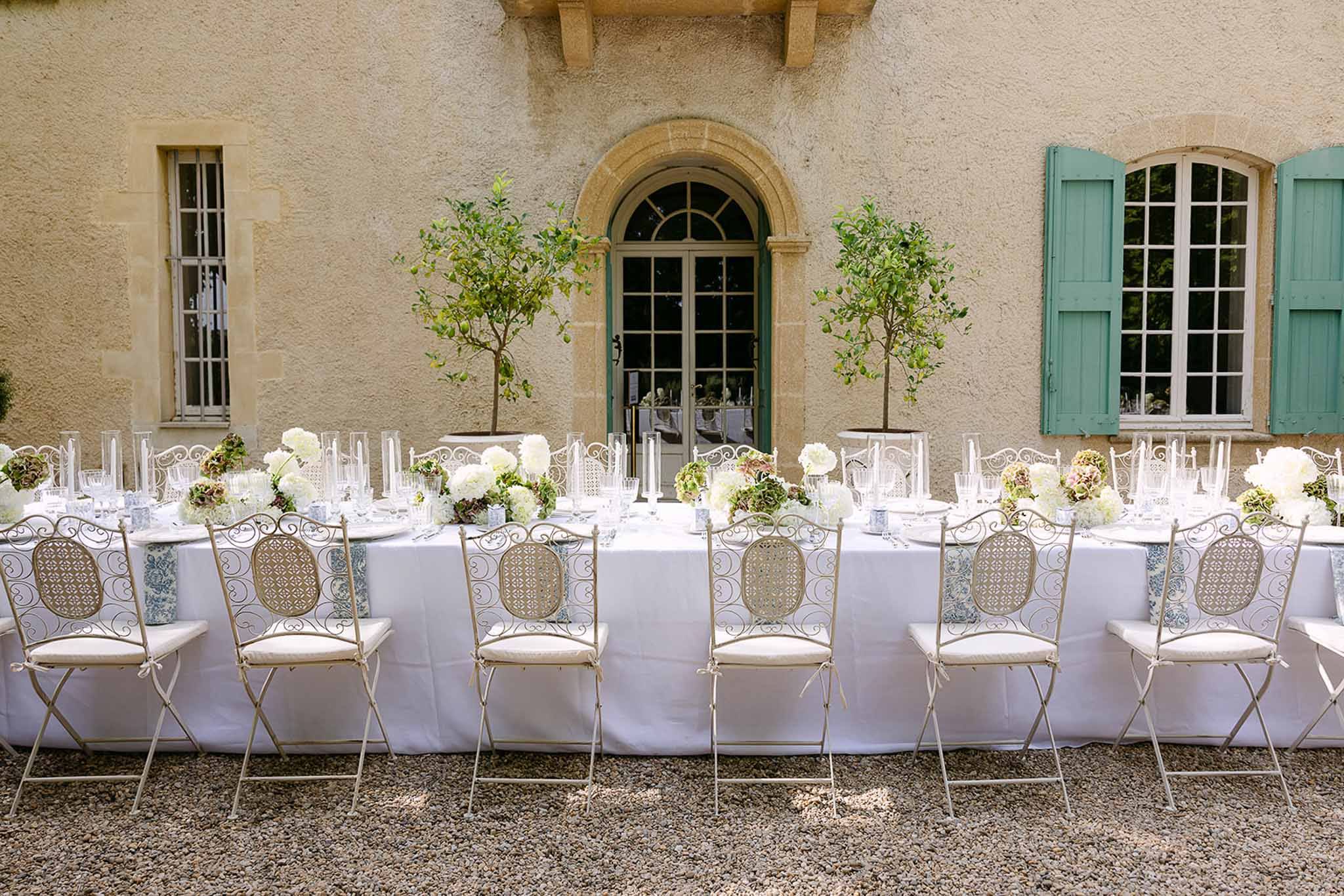 Long table with blue toile runner, hydrangea centerpieces, and citrus topiaries at teal-shuttered bastide
