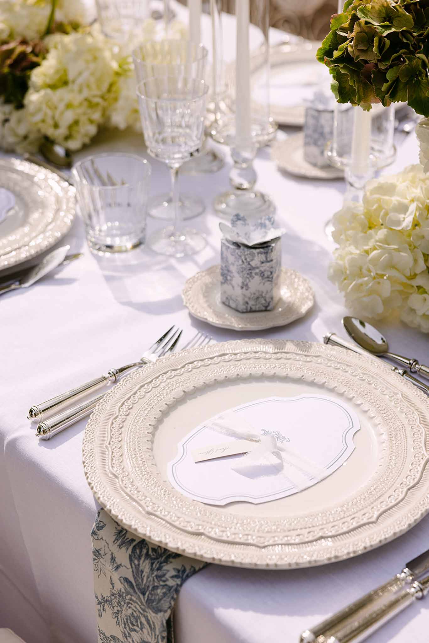 Ivory charger with ribbon-tied menu card, toile de Jouy napkin, silver candles, and white hydrangea arrangements