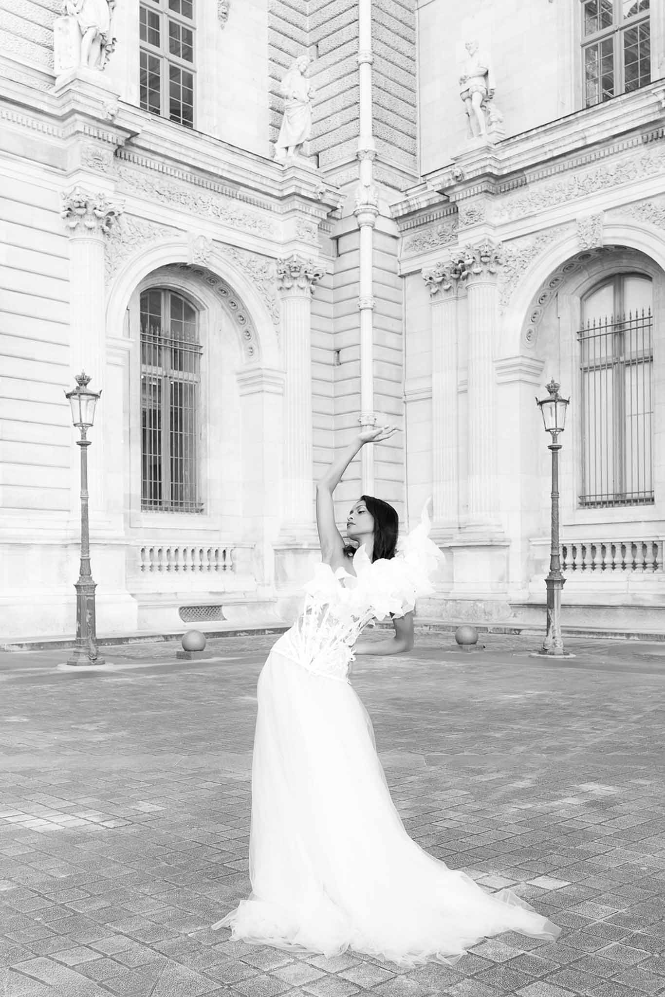 Black and white bride in sculptural tulle gown posing ballet-style in Parisian classical courtyard