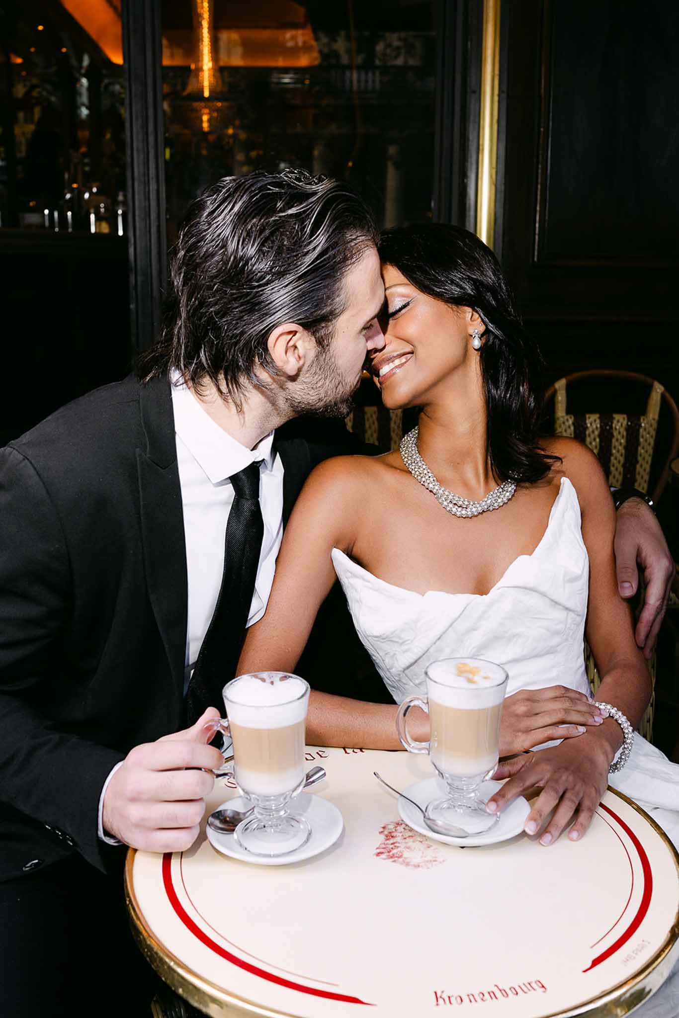 Bride and groom leaning foreheads together at Parisian cafe table with latte glasses