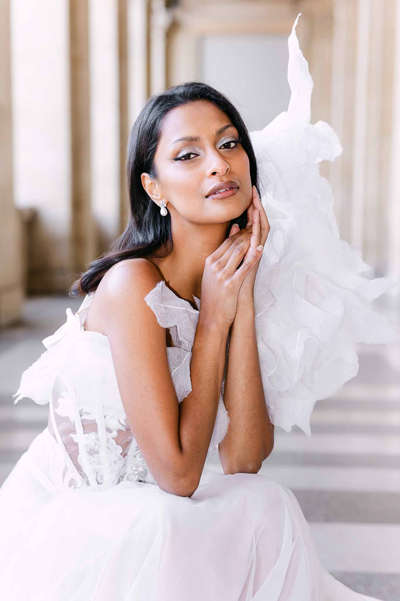 Bride in strapless white lace corset gown with organza ruffle details seated in classical stone arcade