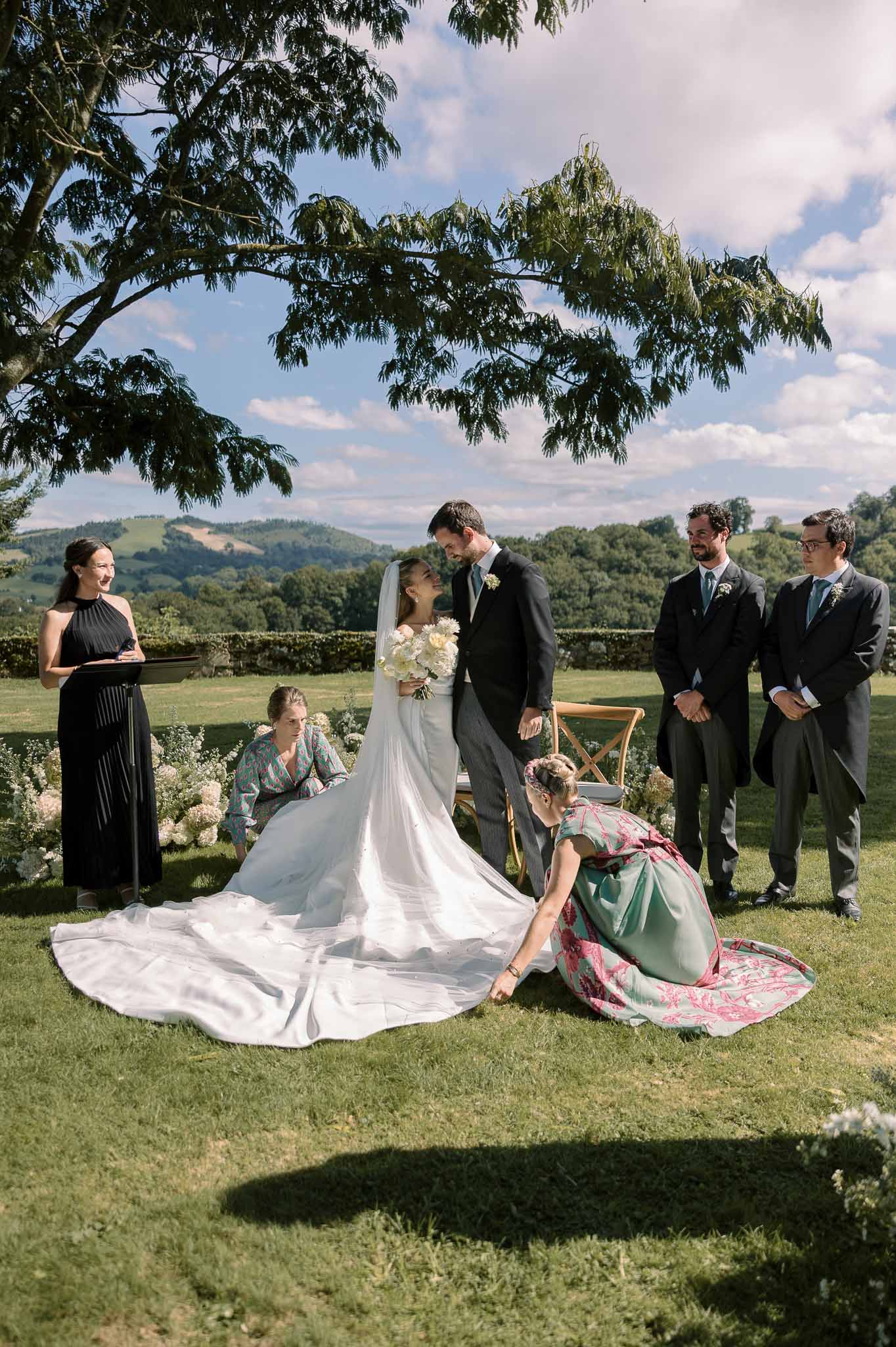 Outdoor ceremony on lawn with bride in long-sleeve gown and cathedral train beside groom and groomsmen