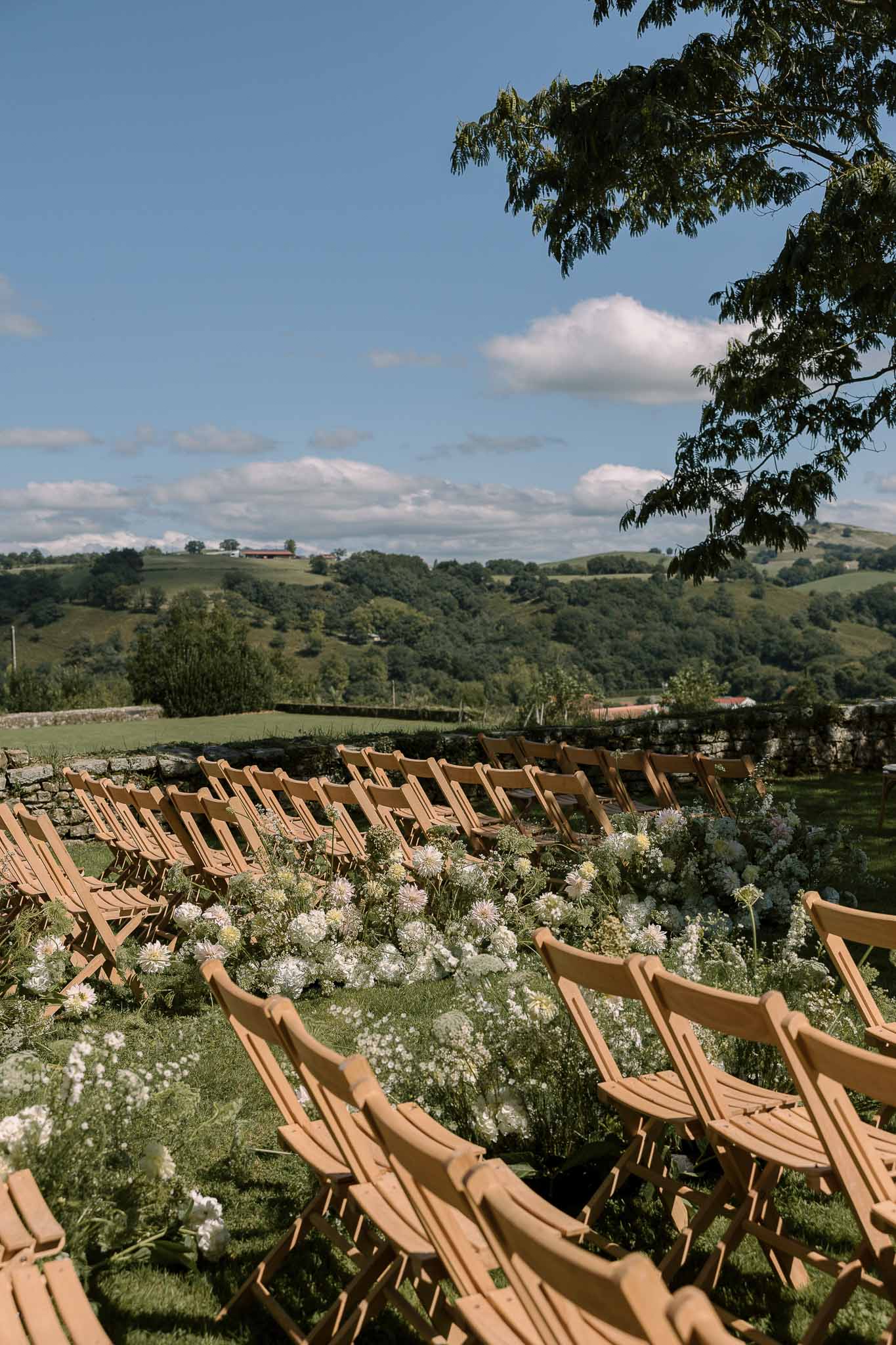 Ceremony setup with wood folding chairs and wildflower ground arrangements on grass terrace