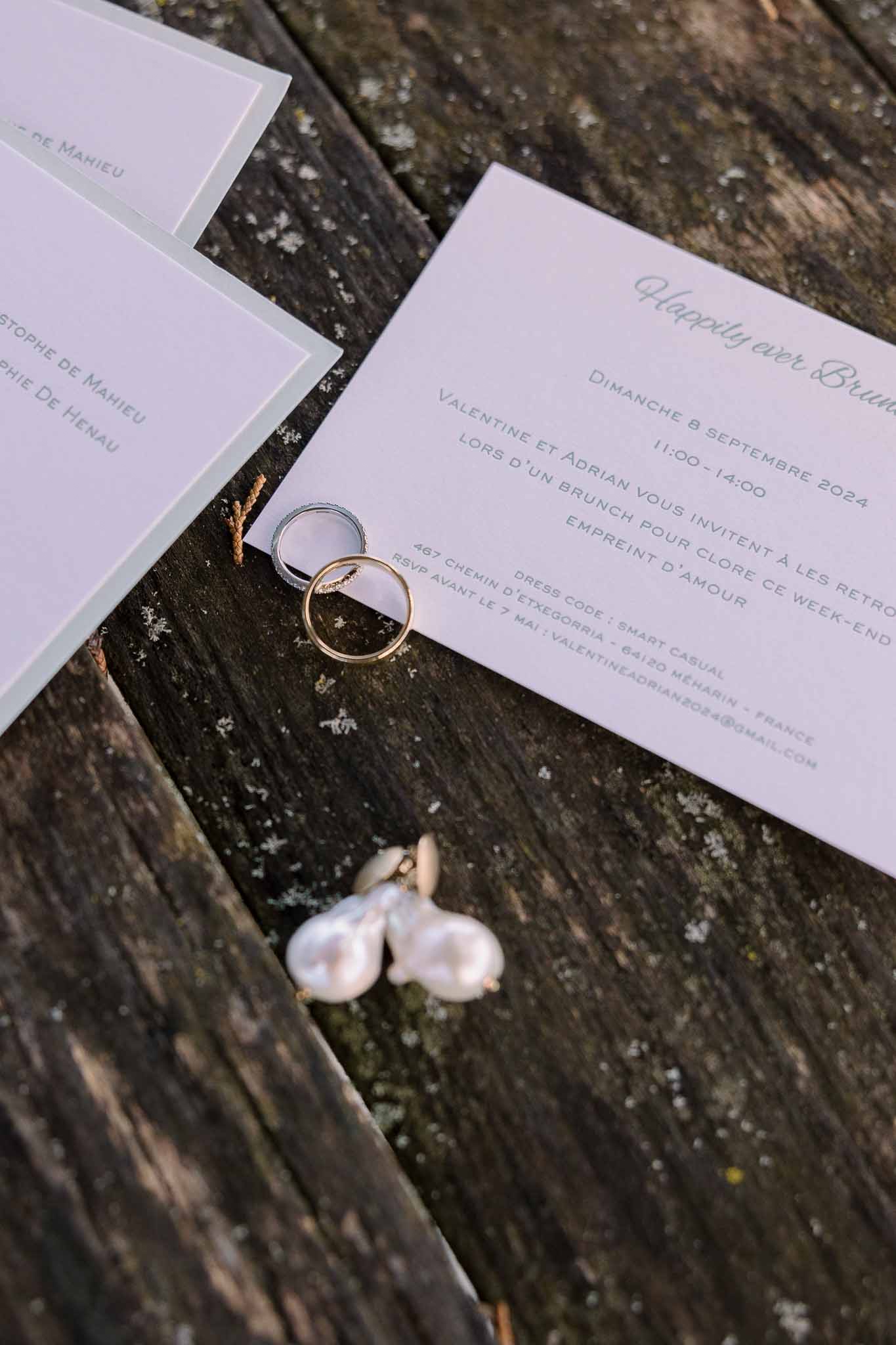 Sage-bordered stationery suite with gold and silver wedding bands and baroque pearl earrings on wood