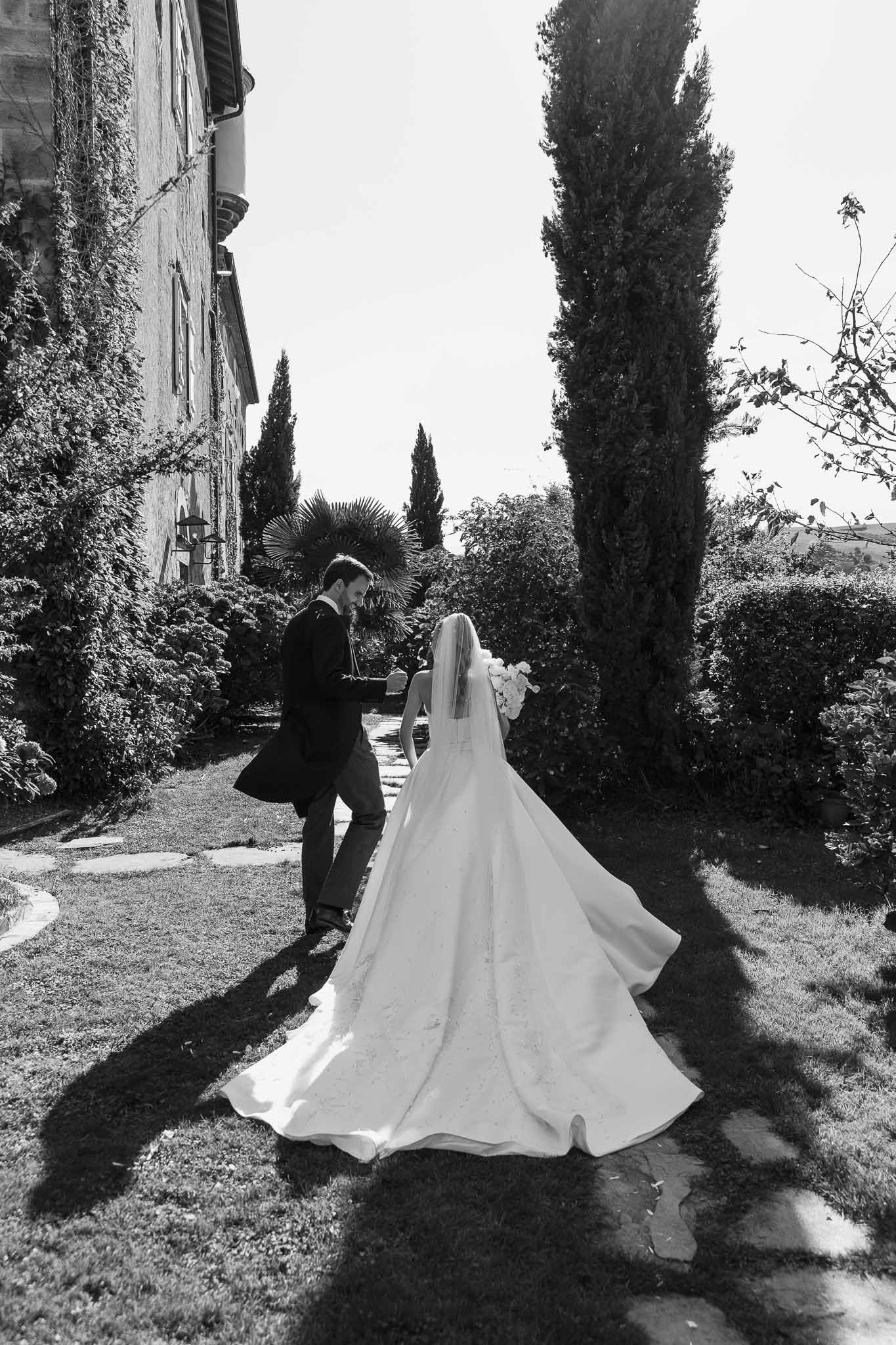 Black and white couple walking from behind bride with ball gown cathedral train and bouquet at manor grounds