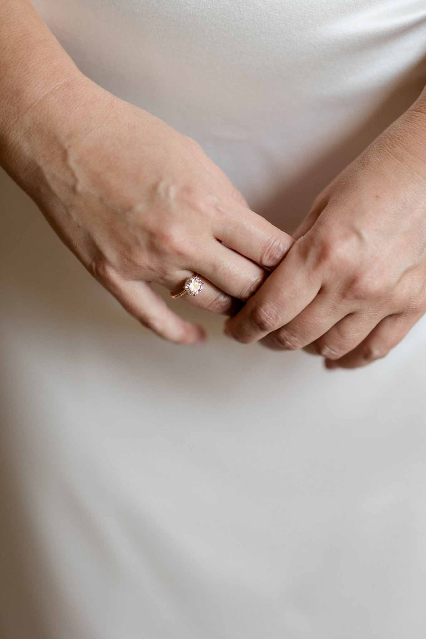 Close-up of bride's hands on ivory satin dress showing yellow gold diamond halo engagement ring