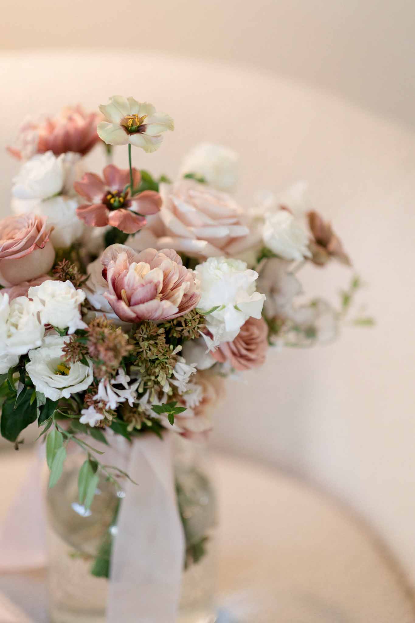 Close-up of bridal bouquet with dusty rose garden roses, mauve tulips, and white lisianthus in glass vase