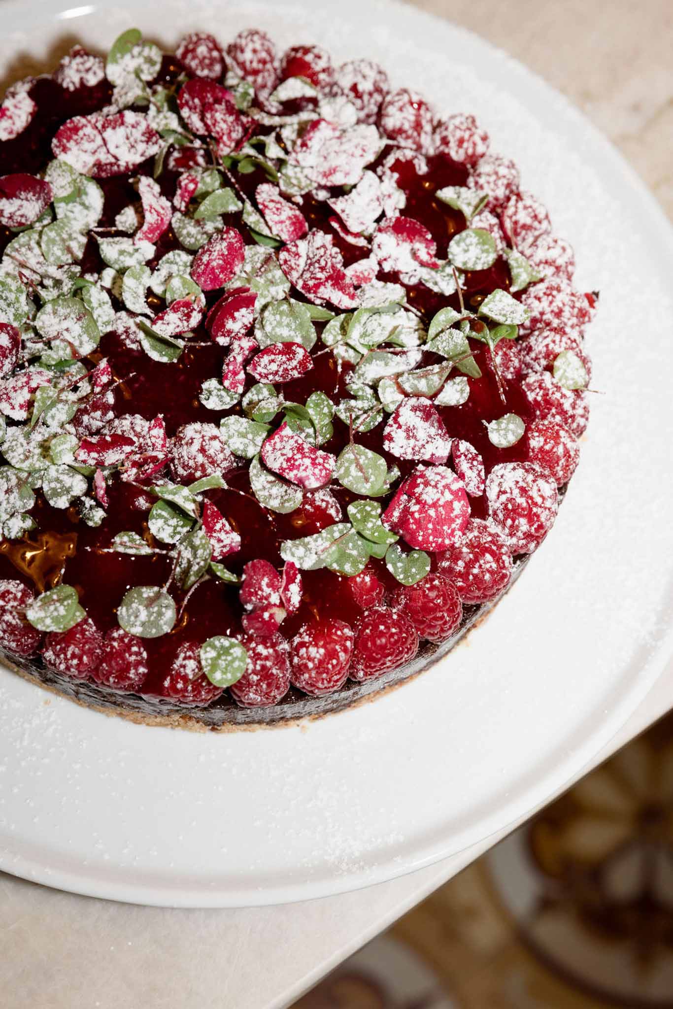 Close-up of wedding dessert tart with red fruit glaze and fresh raspberries on white ceramic cake stand