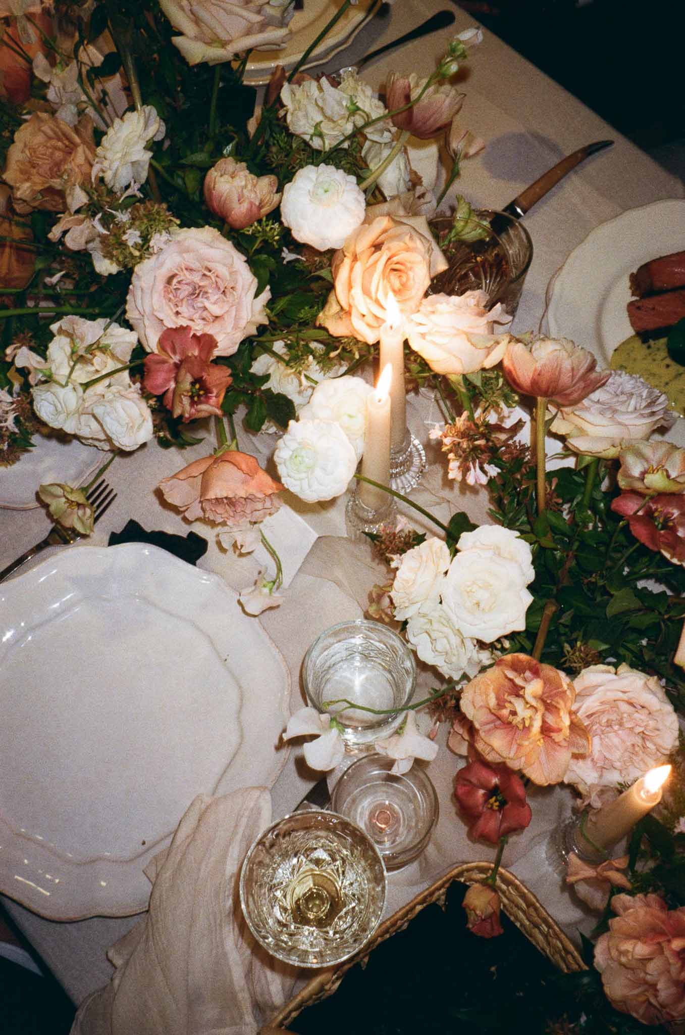 Overhead reception tablescape with blush and peach roses terracotta ranunculus ivory candles and scallop-edged china