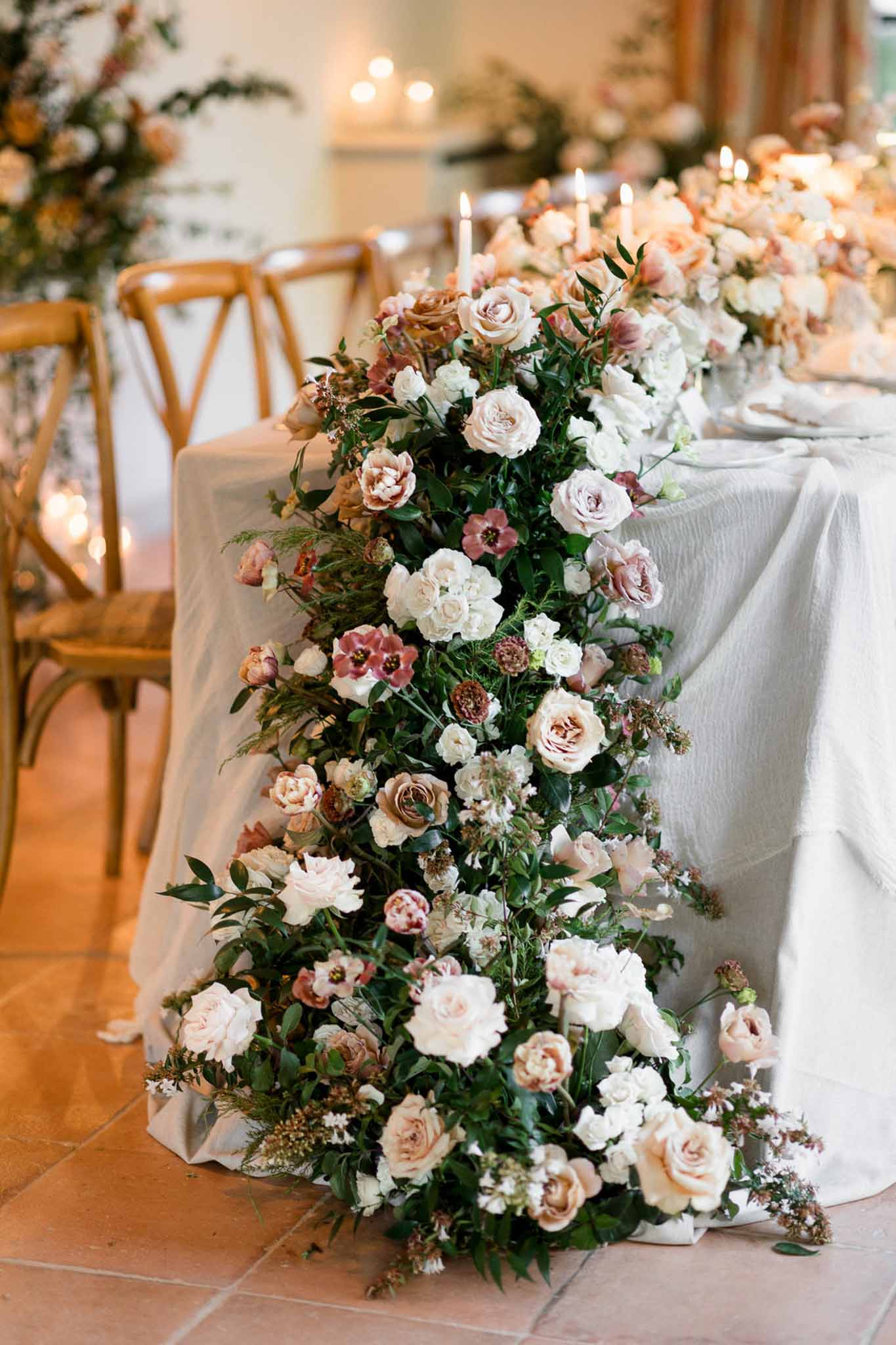 Cascading centerpiece of blush mauve and antique roses with taper candles spilling to terracotta floor