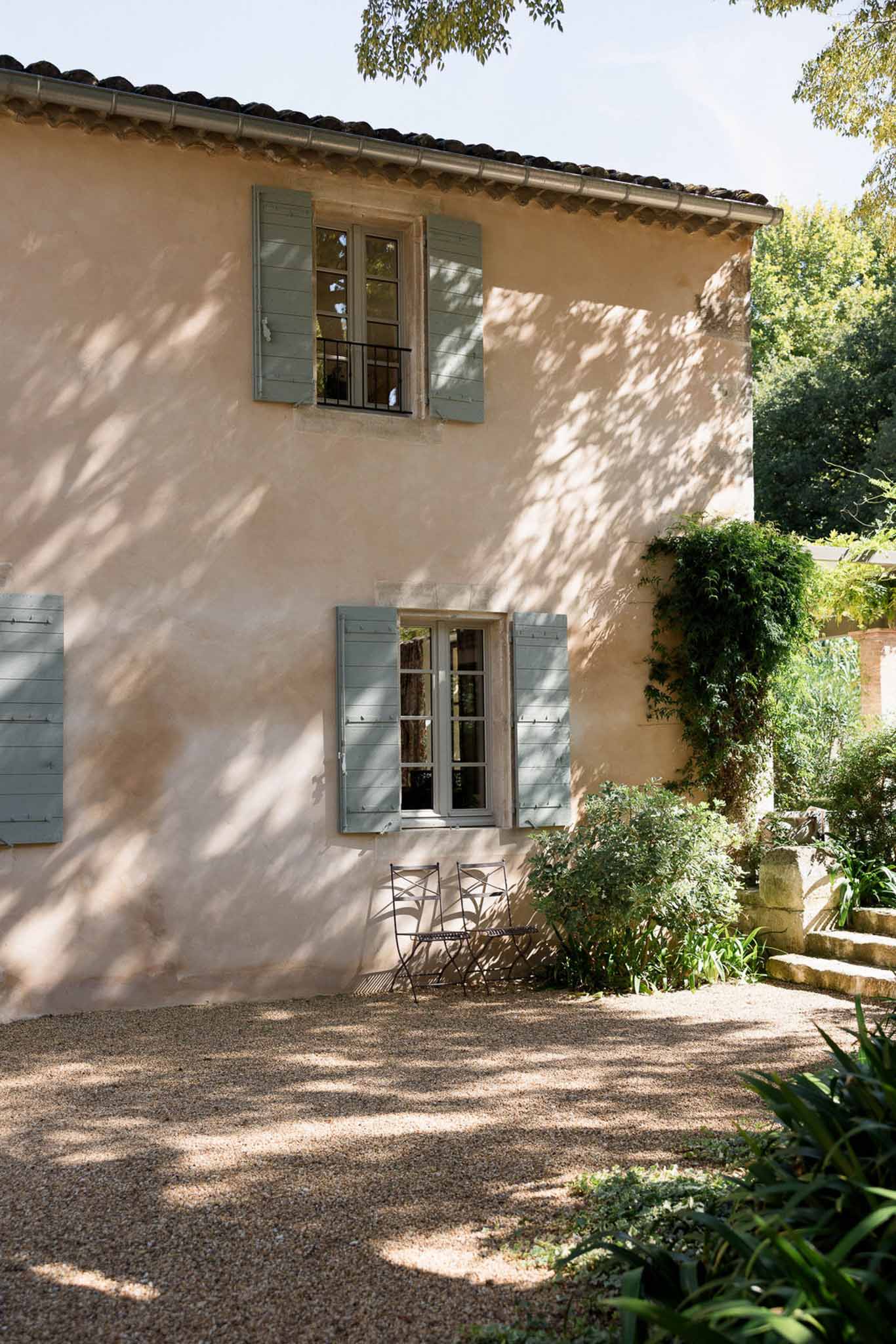 Provencal mas with terracotta-pink walls, sage green shutters, and climbing greenery on gravel courtyard