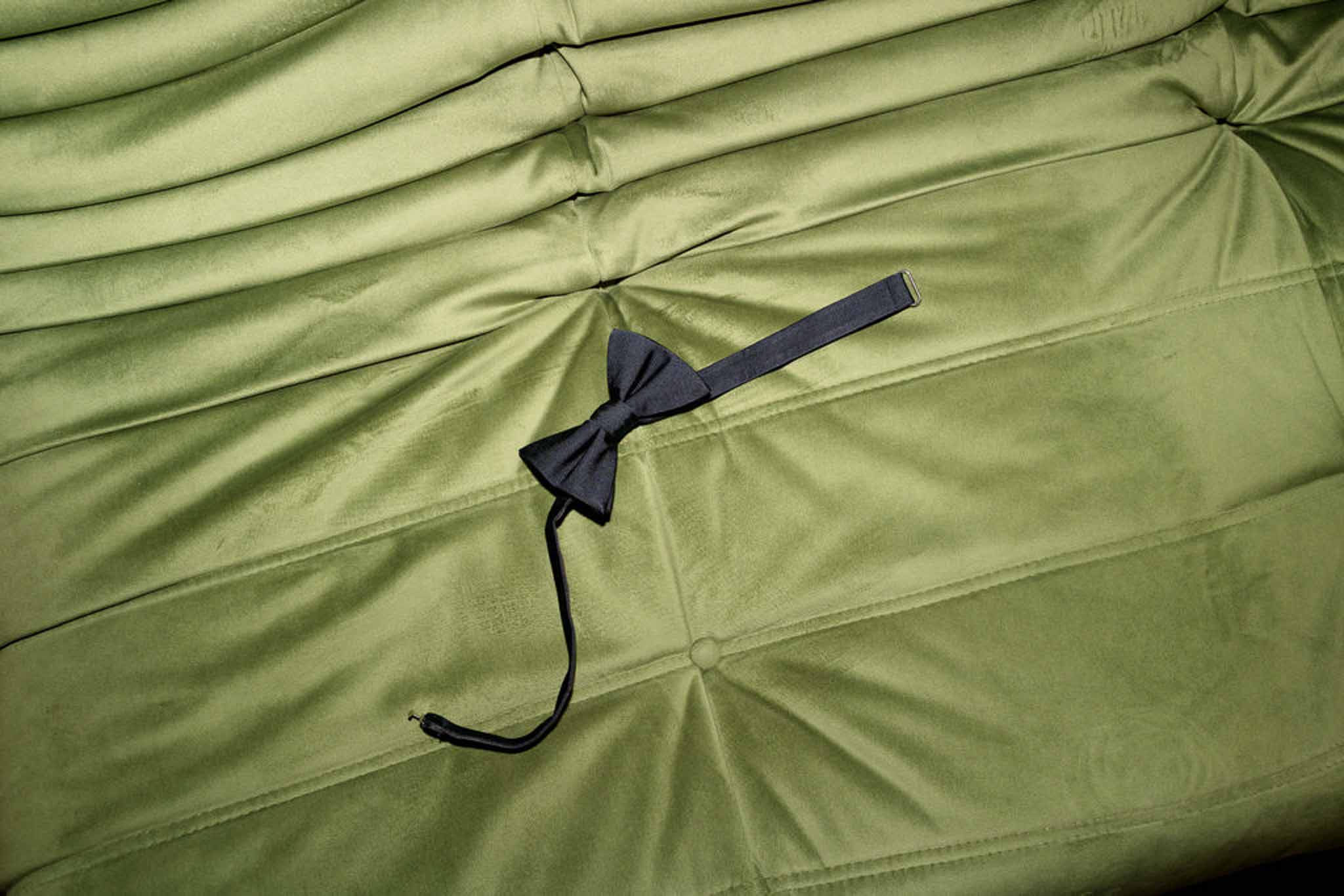 Navy bow tie resting on olive green tufted velvet surface during groom preparations