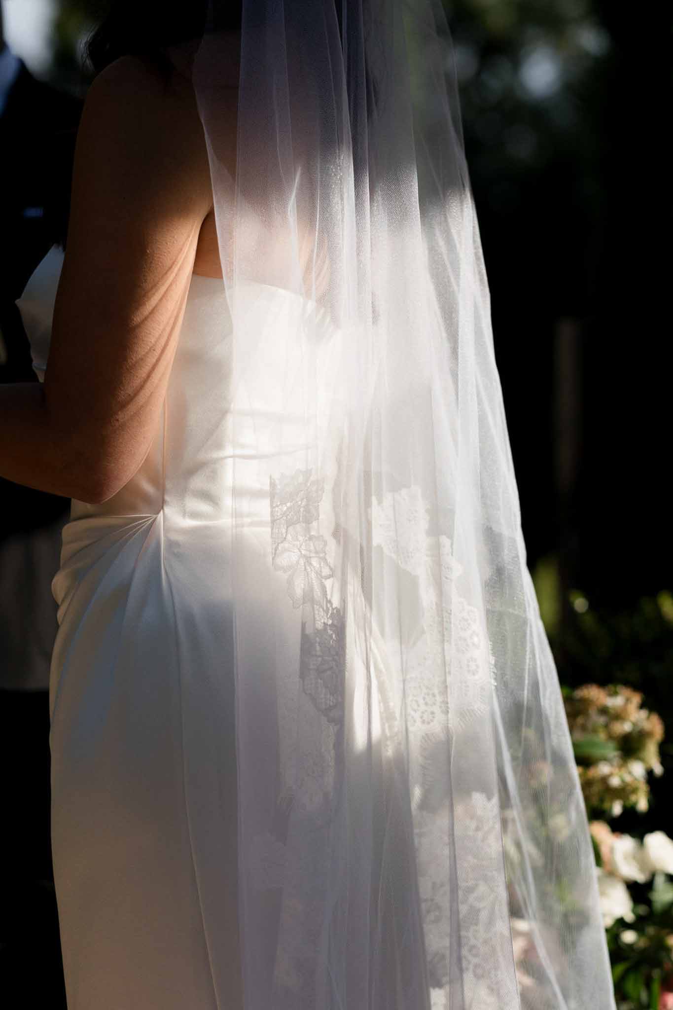 Close-up of backlit tulle veil over ivory satin gown showing lace applique detail