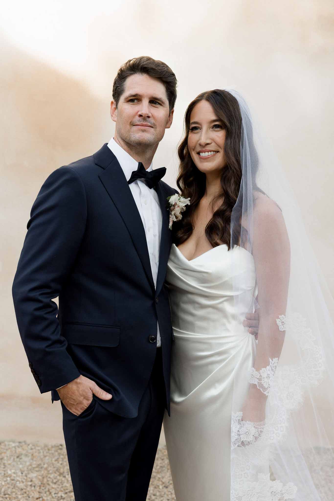 Mid-length couple portrait bride in strapless satin gown with lace-trimmed cathedral veil groom in navy tuxedo